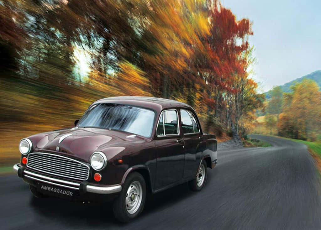 Hindustan Motors 桌布 壁紙 — 一輛栗色Ambassador汽車在蜿蜒的道路上疾馳，穿過色彩繽紛的秋樹，帶有模糊的動態效果。