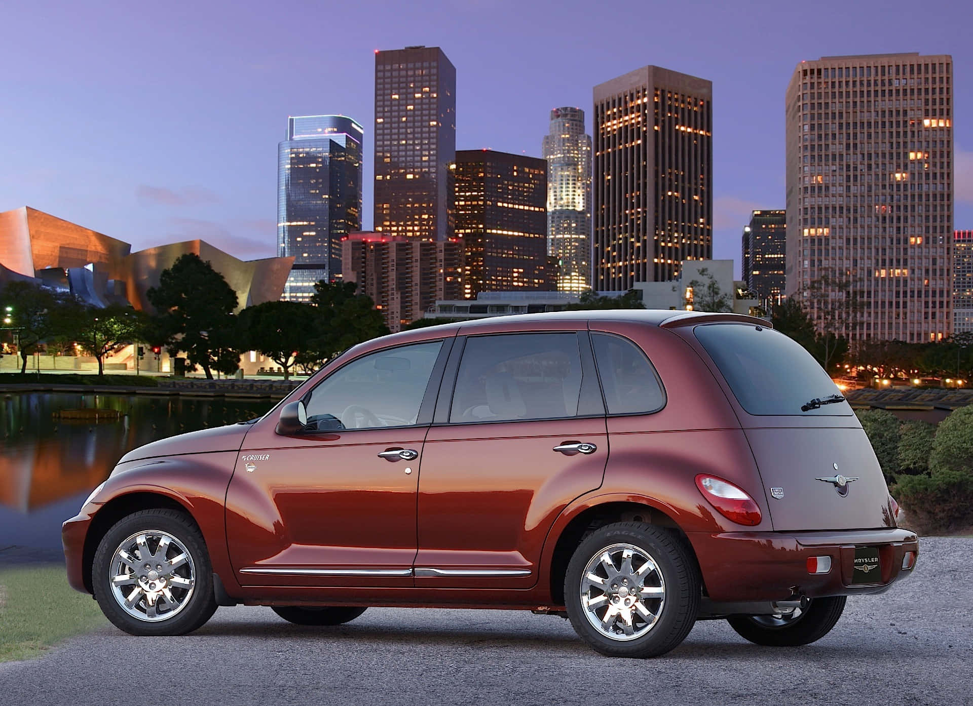 Chrysler Pt Cruiser 桌布 壁紙 — 一輛栗色PT Cruiser停泊在水邊，背後是黃昏時分燈火通明的城市天際線。