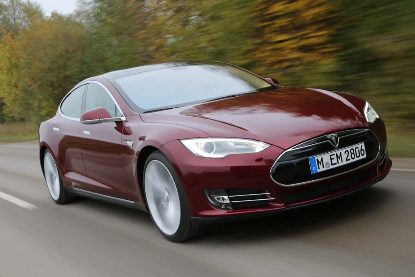 特斯拉 桌布 壁紙 — 一輛栗色Tesla Model S在道路上飛馳，背景中秋天的樹木模糊不清。