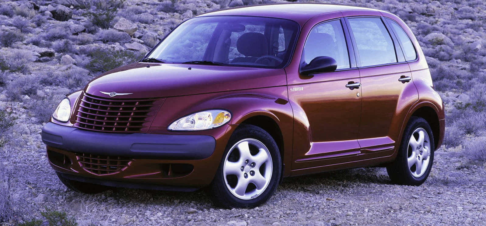 Chrysler Pt Cruiser 桌布 壁紙 — 一輛栗色克萊斯勒 PT Cruiser 停泊在岩石沙漠地形上，天空呈現柔和的紫色。