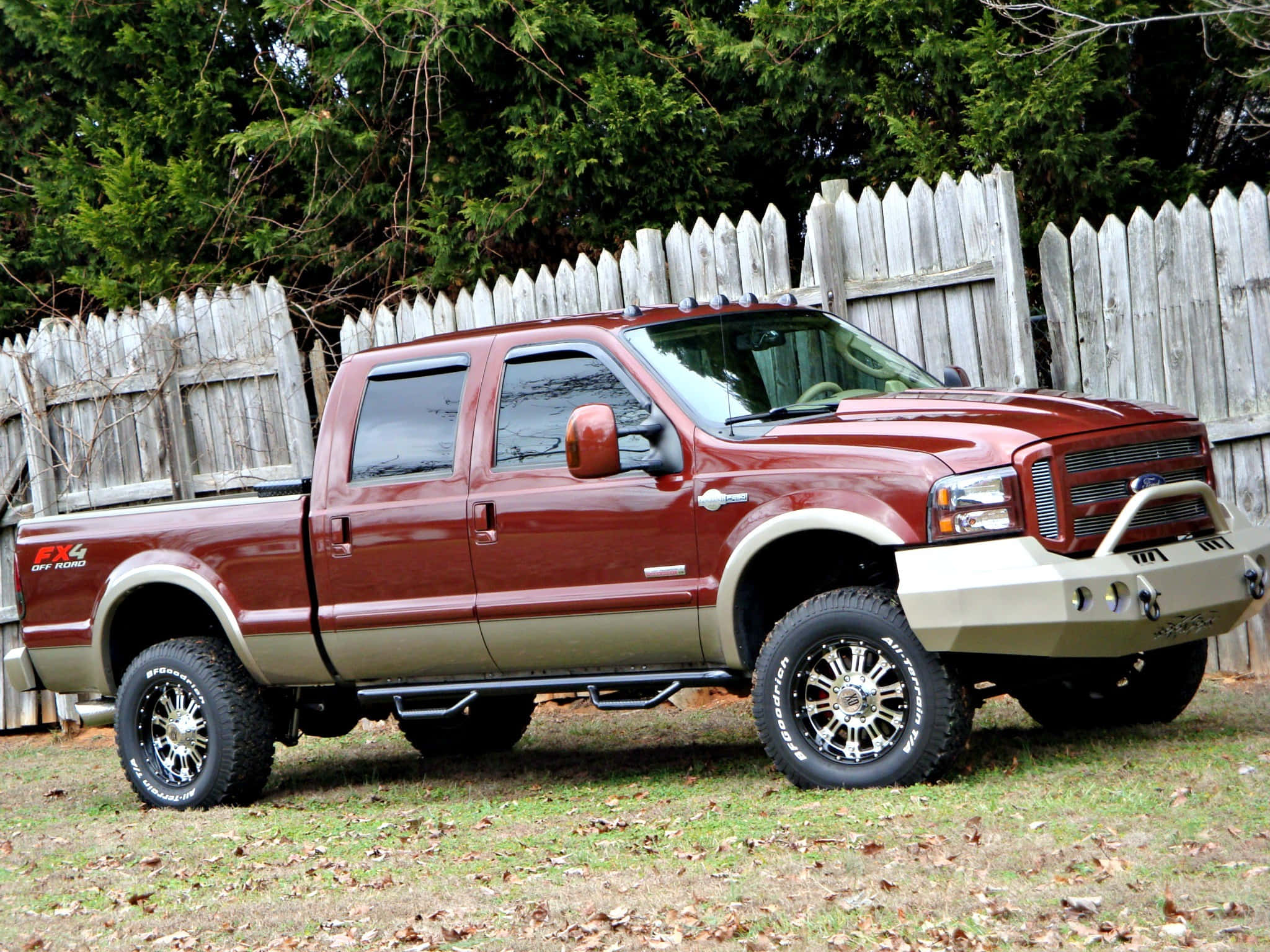 Pickup Truck 桌布 壁紙 — 一輛栗色升高版福特F-150 FX4皮卡車，配備鍍鉻輪圈和米色前保險桿，停在草地上，靠近一道風化的白色尖樁籬笆。