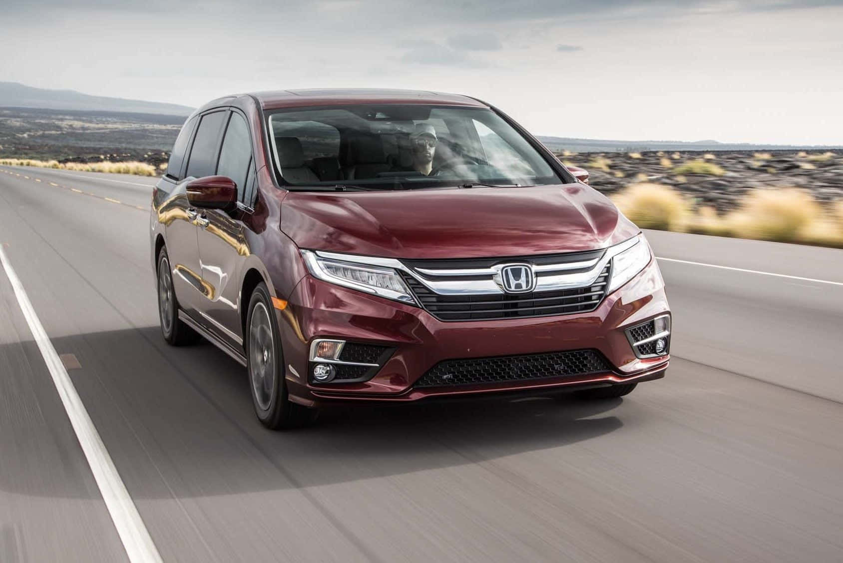 Honda Odyssey 桌布 壁紙 — 一輛栗色本田小型貨車在沙漠高速公路上疾馳，周圍環境模糊，遠山在陰天天空下。