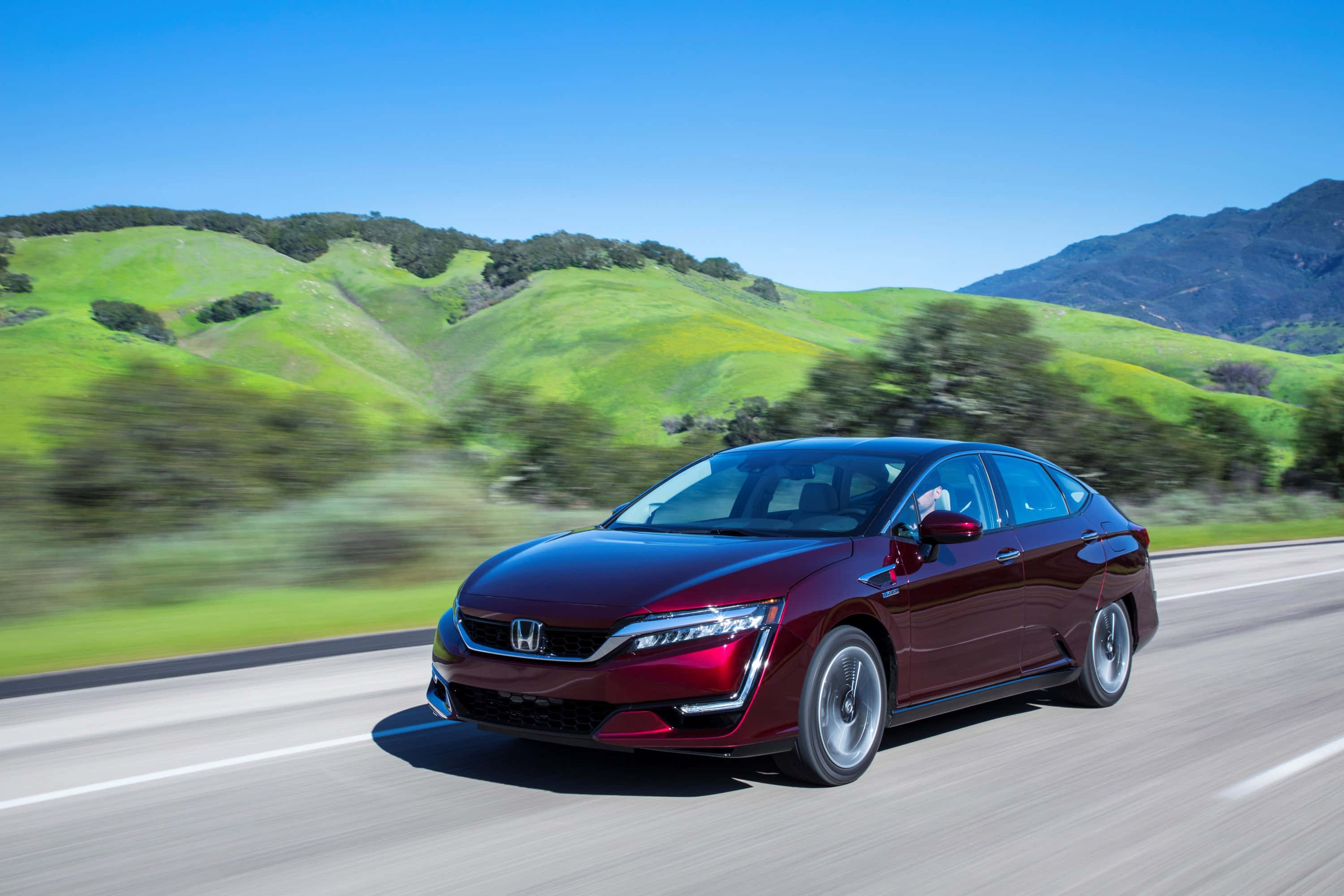 Honda Clarity 桌布 壁紙 — 一輛栗色本田轎車在陽光明媚的高速公路上疾駛，背景是模糊的綠色山丘和藍天。