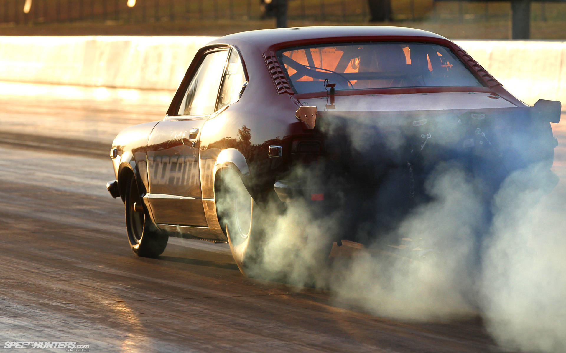 Racing 桌布 壁紙 — 一輛栗色經典肌肉車在塵土飛揚的賽道上燒胎，在黃金時段的光線下冒出濃煙。