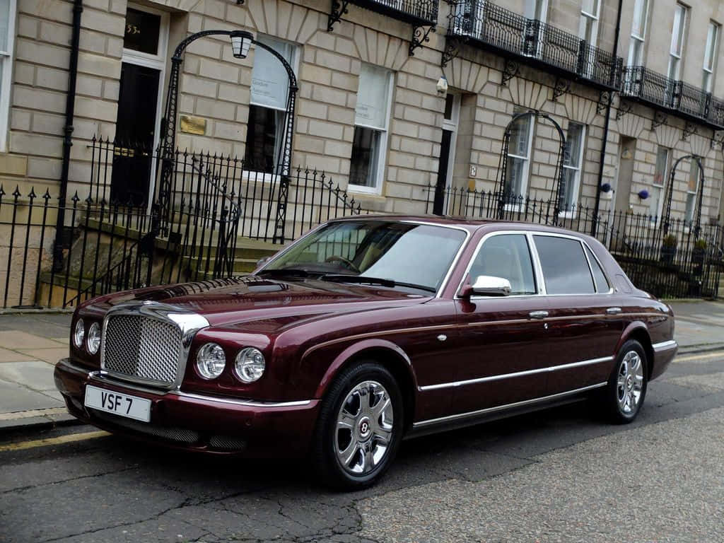 Bentley Arnage 桌布 壁紙 — 一輛栗色賓利Arnage豪華轎車停泊在鵝卵石街道上，旁邊是優雅的石砌聯排別墅，帶有黑色鍛鐵圍欄。