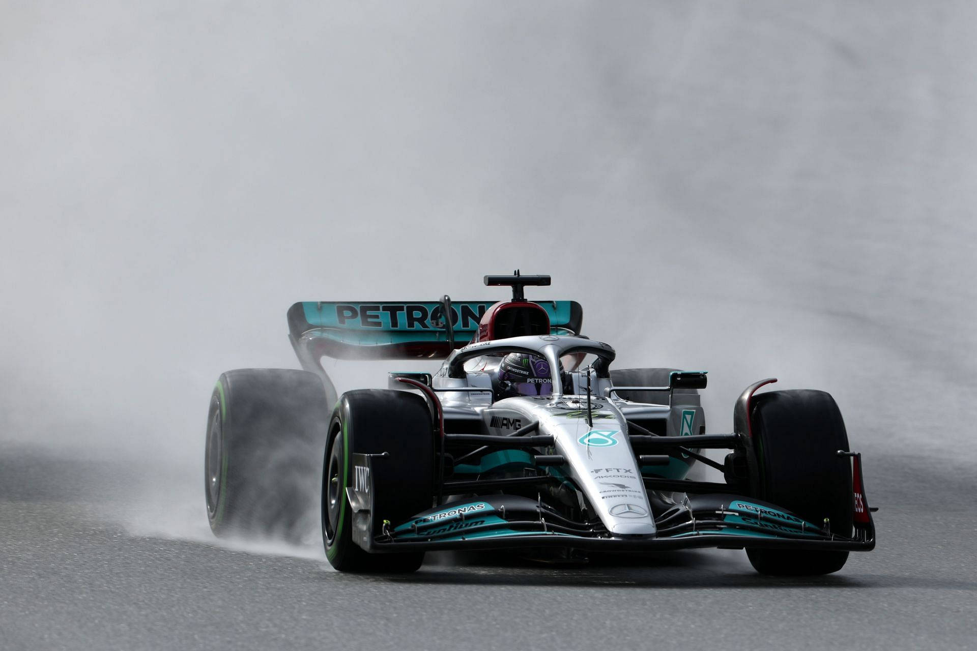 F1 桌布 壁紙 — 一輛梅賽德斯一級方程式賽車在潮濕的賽道上高速駛過霧濛濛的彎道，濺起水花。
