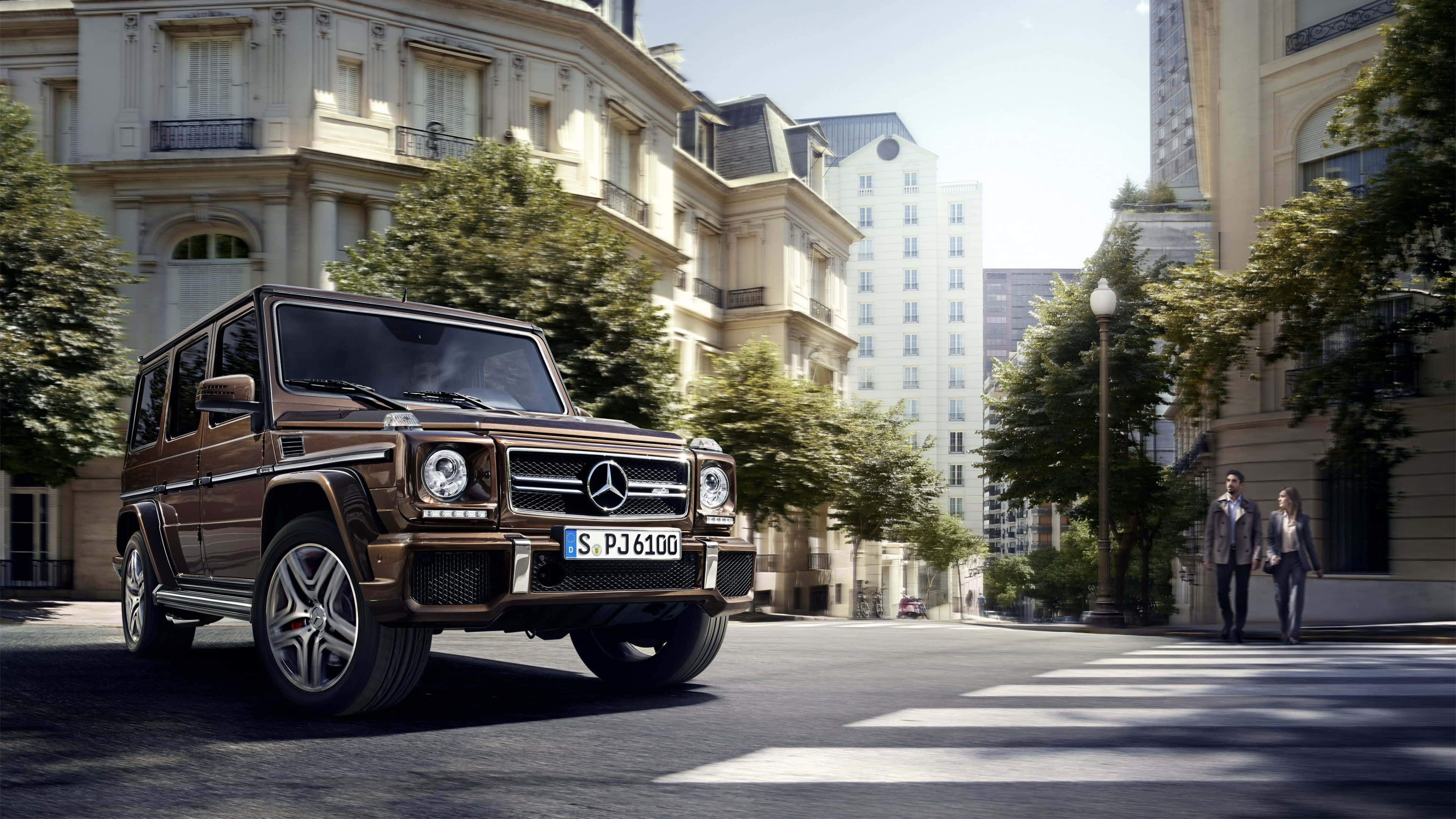 4K 奔馳壁紙 桌布 壁紙 — 一輛棕色 Mercedes G-Class SUV 在明亮的日光下行駛在巴黎一條綠樹成蔭的街道上，有行人和經典建築。