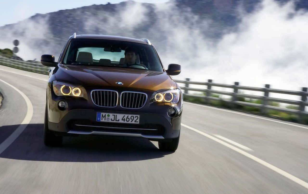 Bmw I8 桌布 壁紙 — 一輛棕色BMW X1 SUV沿著蜿蜒的山路疾馳，山頂周圍有霧氣繚繞。