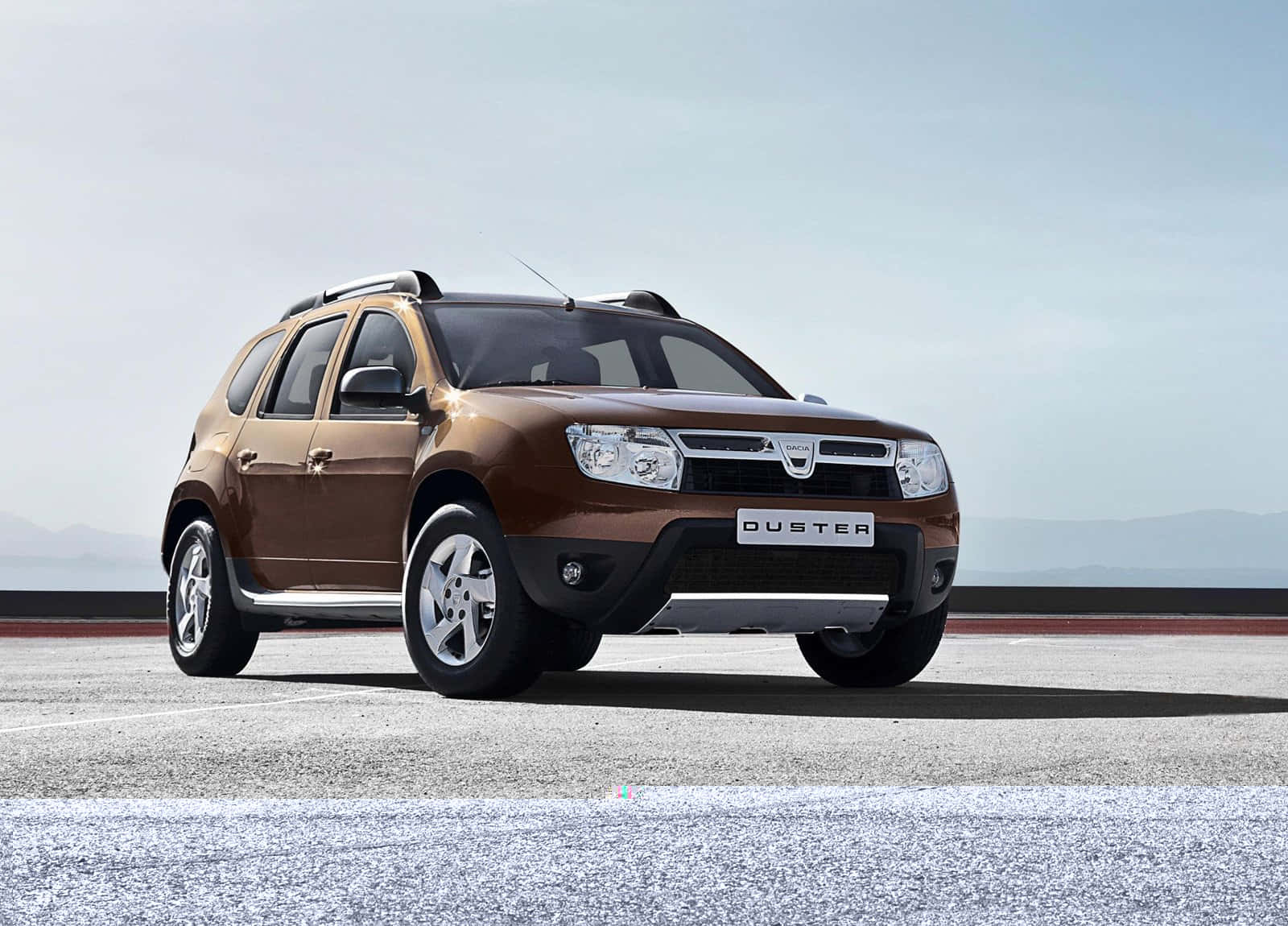 Dacia 桌布 壁紙 — 一輛棕色Duster SUV停在鋪砌路面上，遠山在蒼白天空下若隱若現。
