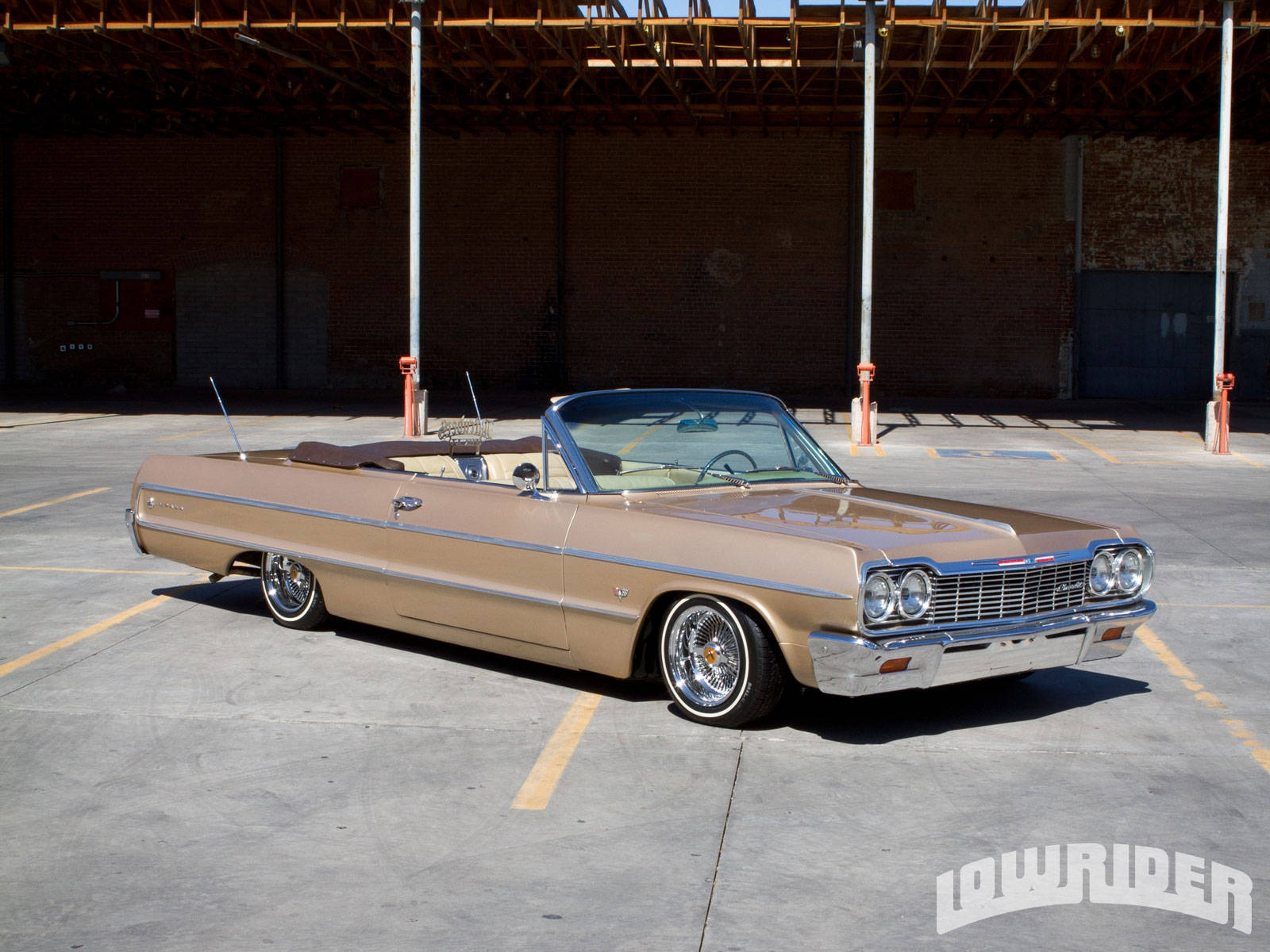 Lowrider 桌布 壁紙 — 一輛棕褐色經典敞篷車，帶有鍍鉻細節，停放在陽光普照的工業用地，上方有木製屋頂結構。