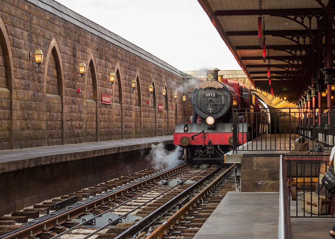 Hogwarts Express 桌布 壁紙 — 一輛標有霍格華茲特快車的蒸汽火車頭冒著煙，抵達宏偉的石造車站月台。