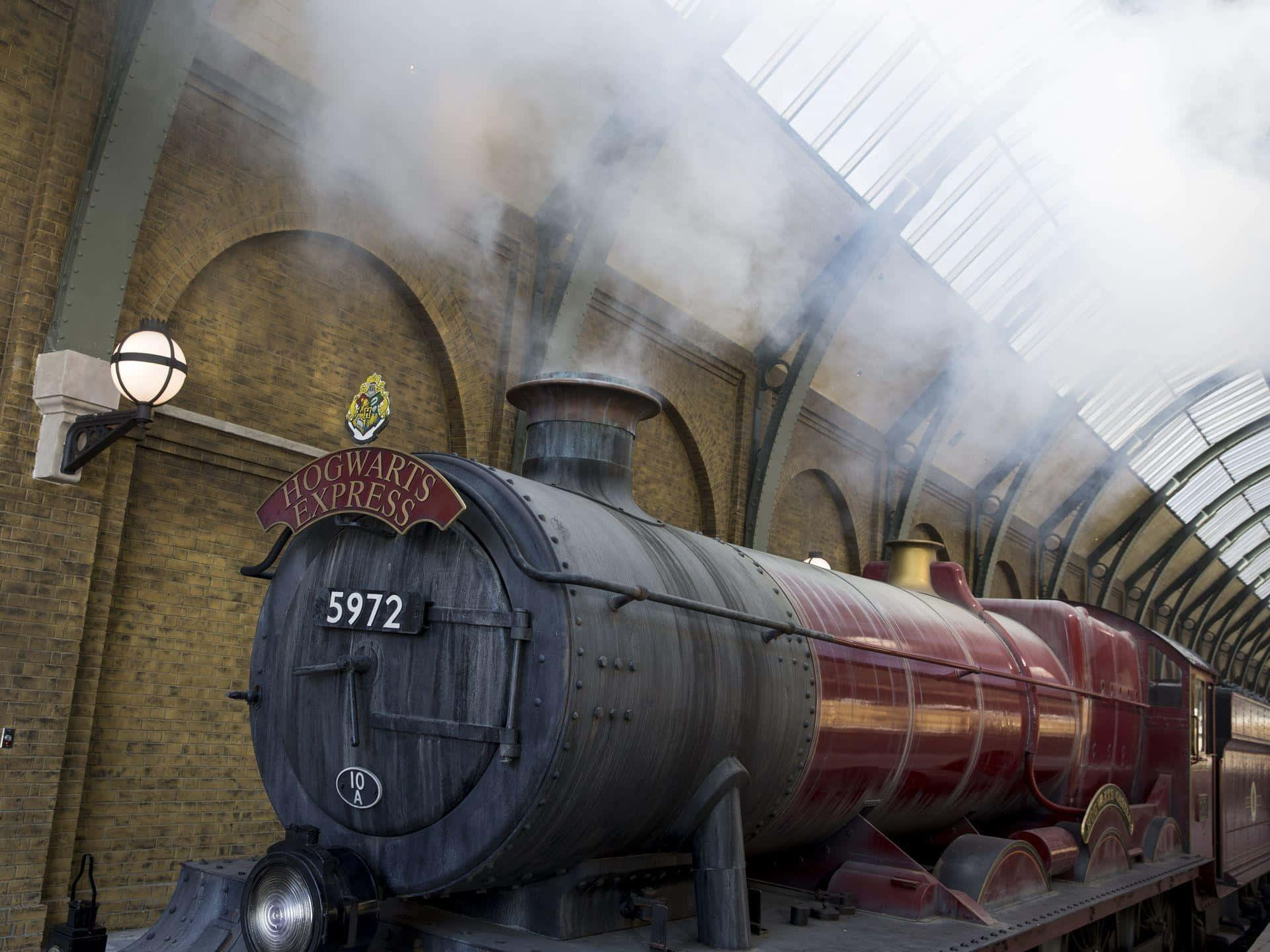 The Hogwarts Express Train 桌布 壁紙 — 一輛標有霍格華茲特快車的雄偉蒸汽火車頭，在一個擁有磚牆和玻璃屋頂的宏偉拱形火車站中噴出煙霧。