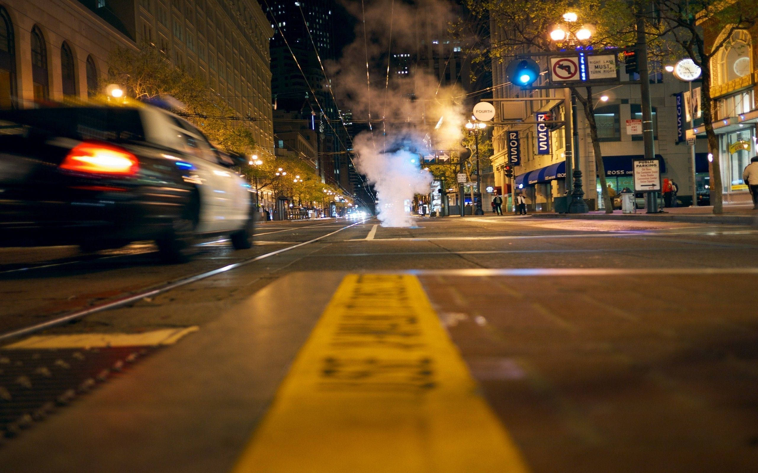 警察 桌布 壁紙 — 一輛模糊的警車在夜間駛過霓虹燈照亮的城市街道，蒸汽從黃色警示帶附近的人行道上升起。