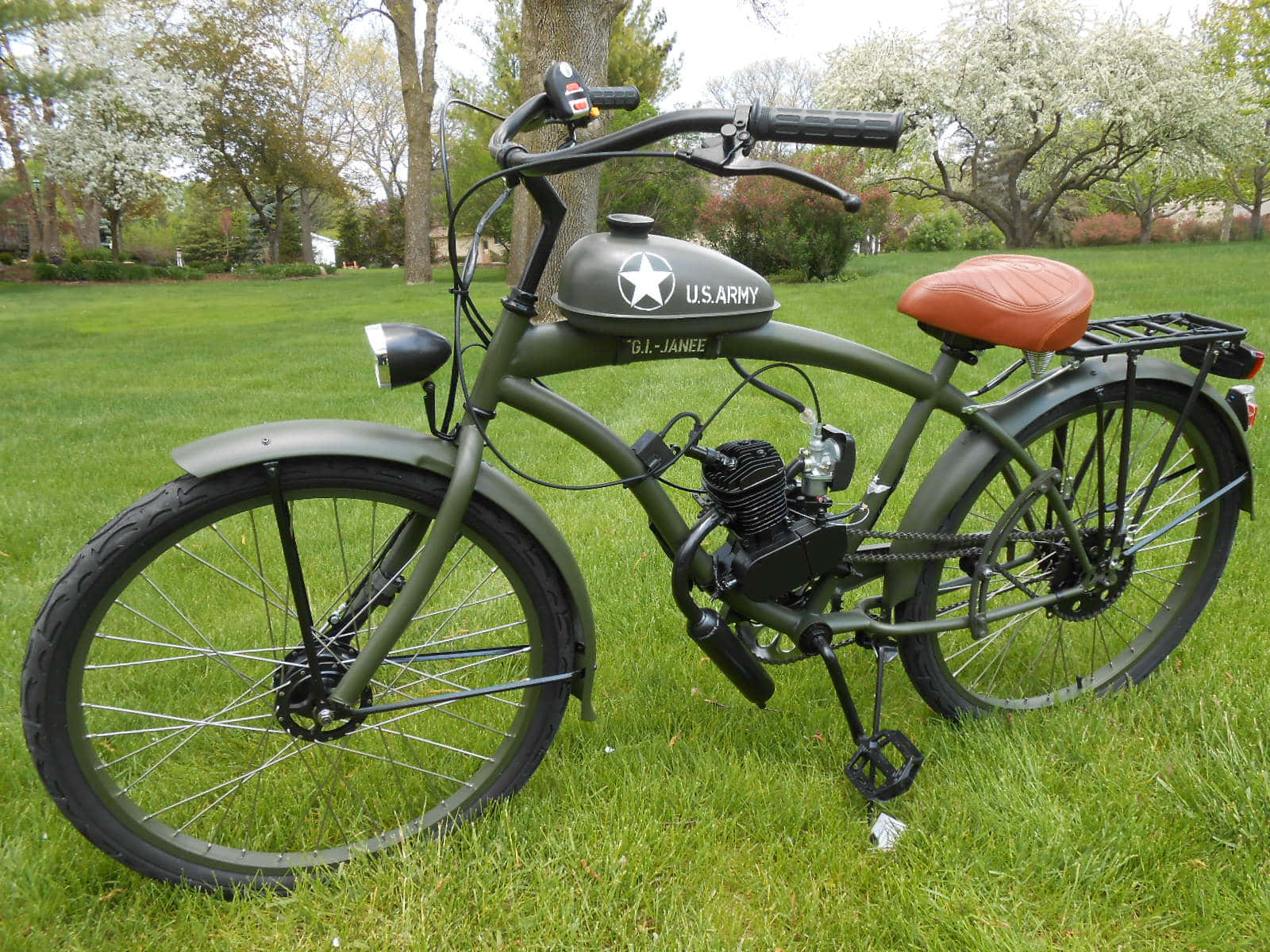 Bicycle 桌布 壁紙 — 一輛橄欖綠軍用風格自行車，帶有美國陸軍油箱和橙色座椅，停放在有開花樹木的草地上。