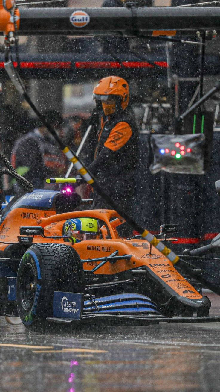 Racing 桌布 壁紙 — 一輛橙色一級方程式賽車正在雨中進行維修，一名身穿橙色裝備的維修站隊員手持水管。