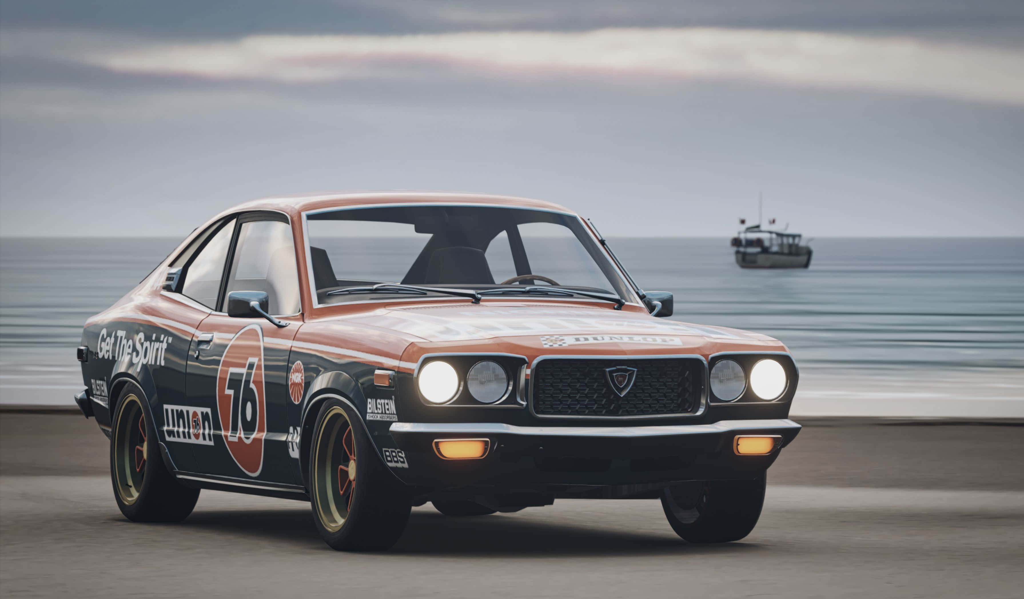 Mazda Rx-3 桌布 壁紙 — 一輛橙色和黑色塗裝的復古賽車沿著海岸公路疾駛，在陰天天空下，地平線上可見一艘船。