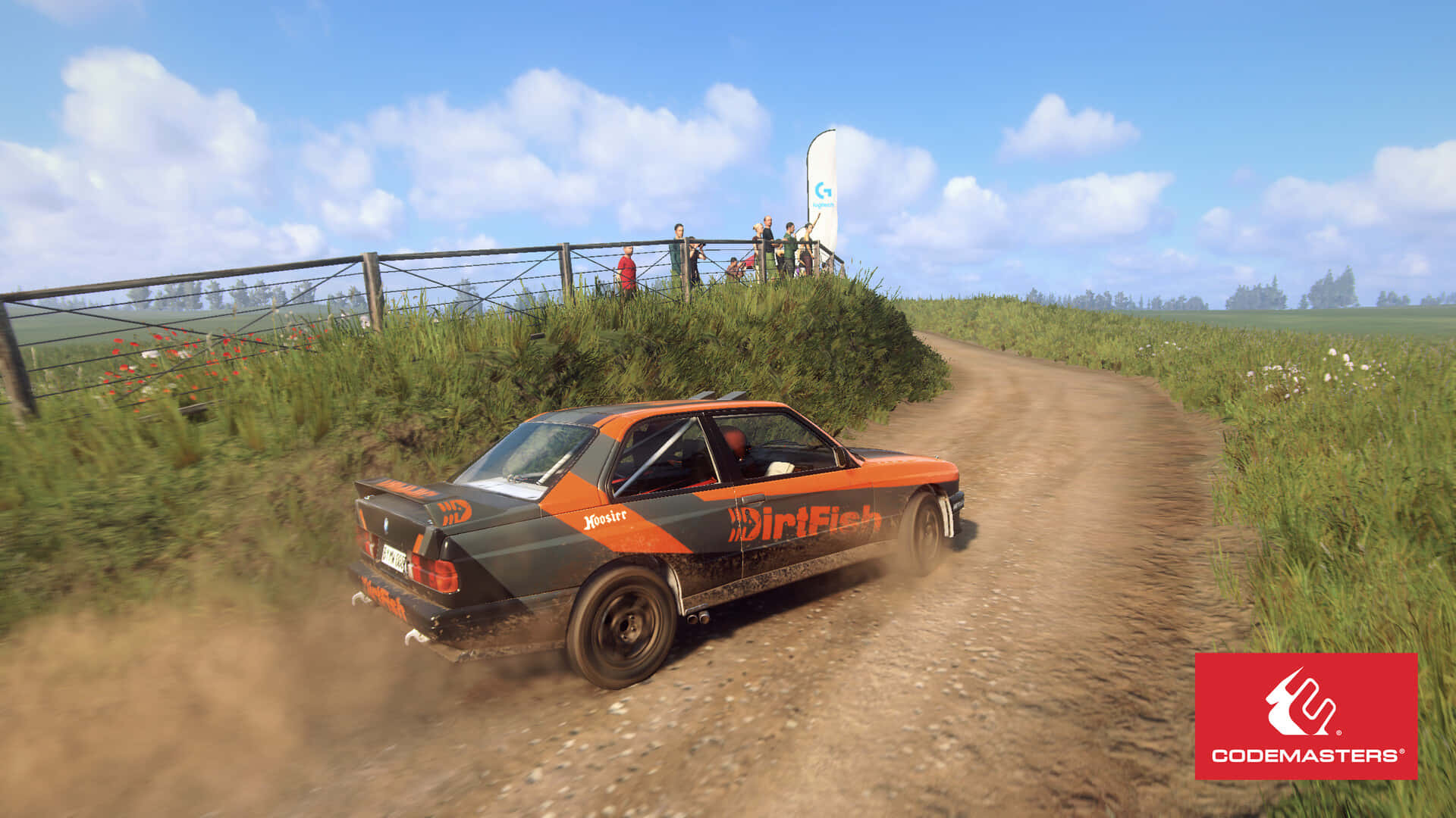 1920x1080 Dirt Rally 桌布 壁紙 — 一輛橙色和黑色的拉力賽車在晴朗藍天下，沿著蜿蜒的泥路穿過草地，揚起塵土。