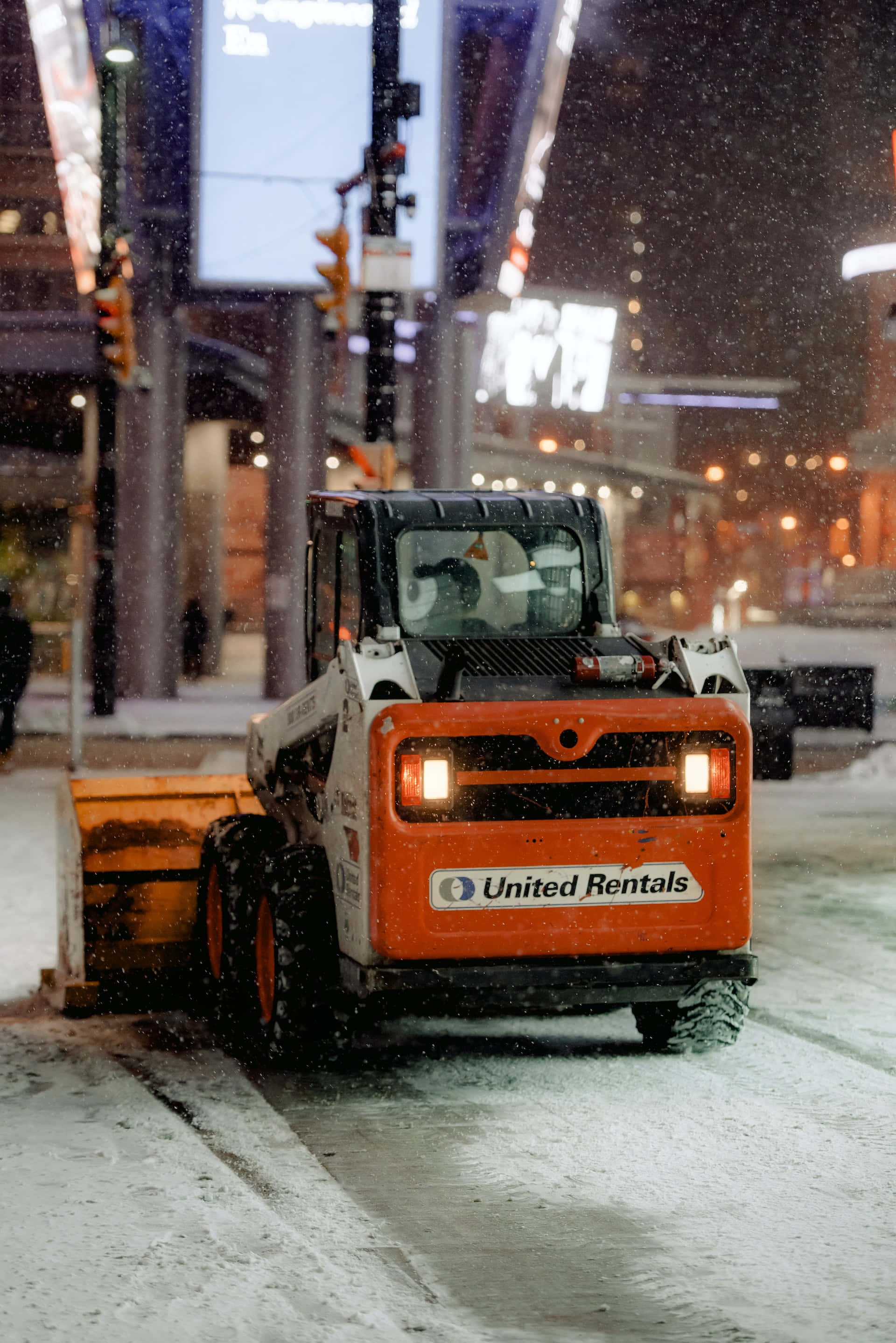 Snowplow 桌布 壁紙 — 一輛橙色掃雪車在夜間清理積雪的市區街道，車頭燈閃爍，雪花飄落。