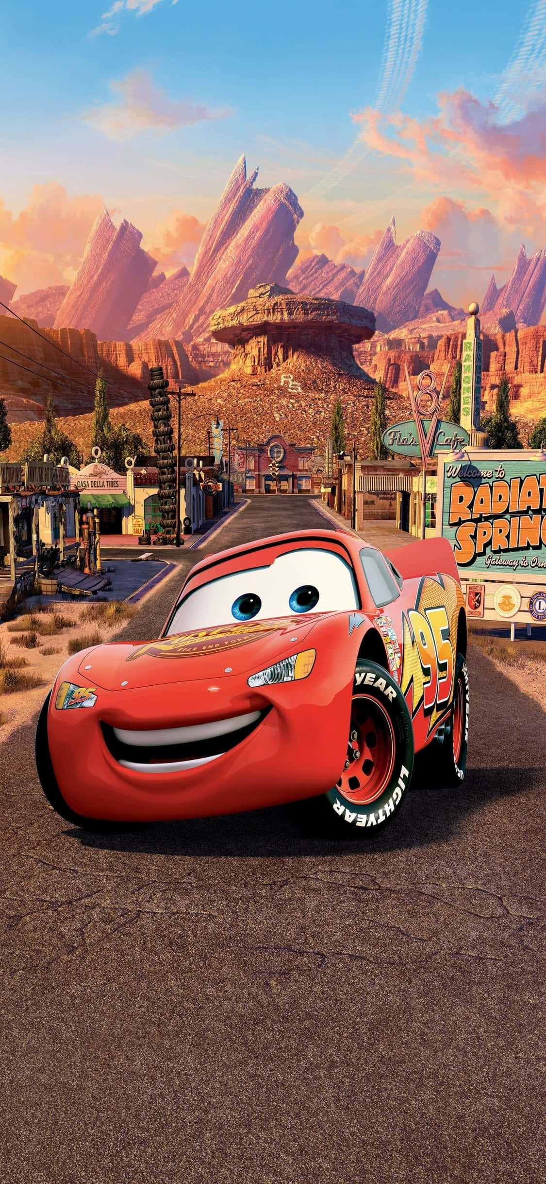 Lightning Mcqueen 桌布 壁紙 — 一輛歡快的紅色賽車在日落時分的沙漠小鎮中自豪地微笑，背景是岩石山脈。