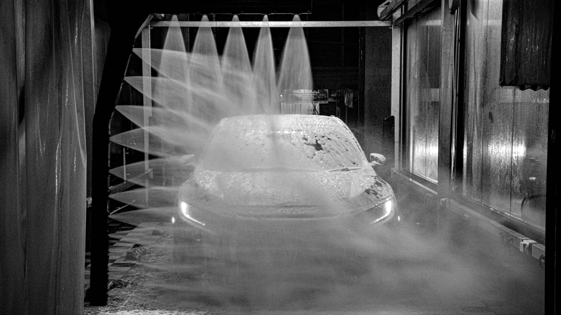 Wash 桌布 壁紙 — 一輛汽車在夜間光線昏暗的自動洗車場中被強力水柱沖洗。