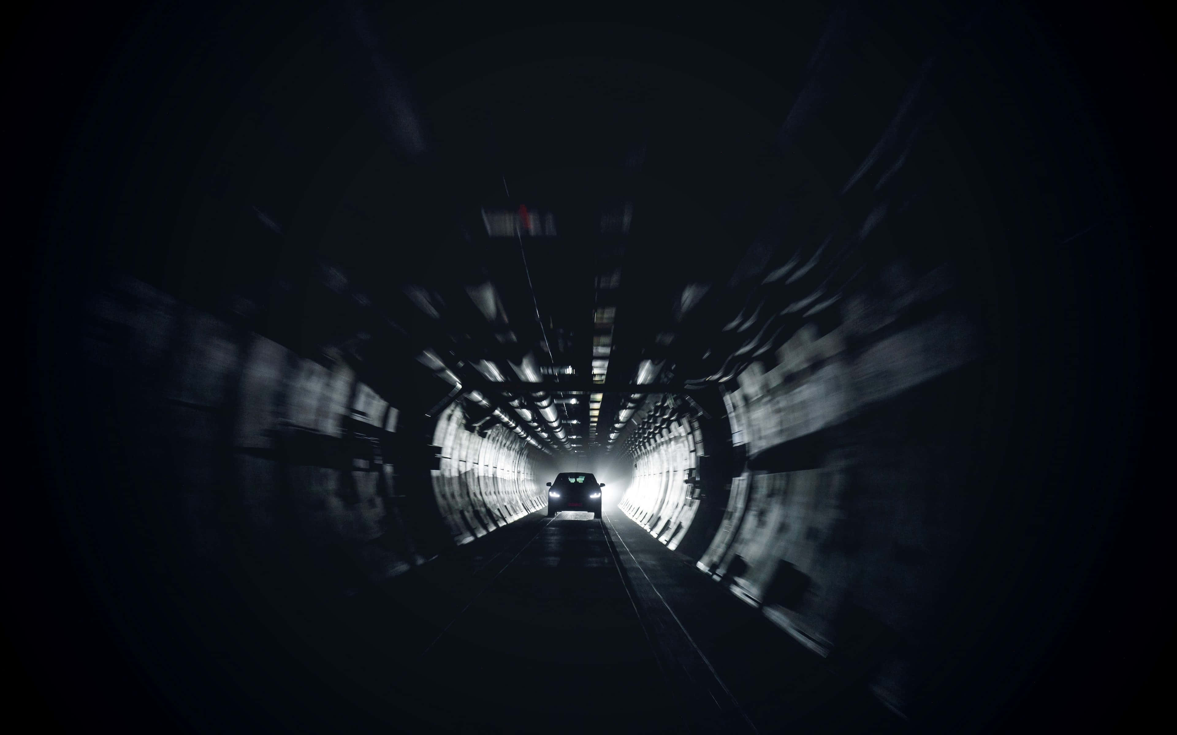 Dark Underground 桌布 壁紙 — 一輛汽車在黑暗的隧道中高速行駛，動態模糊沿著牆壁延伸，朝向前方明亮的出口。
