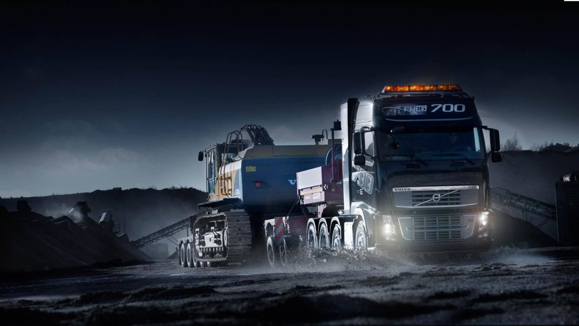 Trucks 桌布 壁紙 — 一輛沃爾沃礦用卡車亮著車頭燈，在夜間駛過黑暗的工業採石場，揚起灰塵。