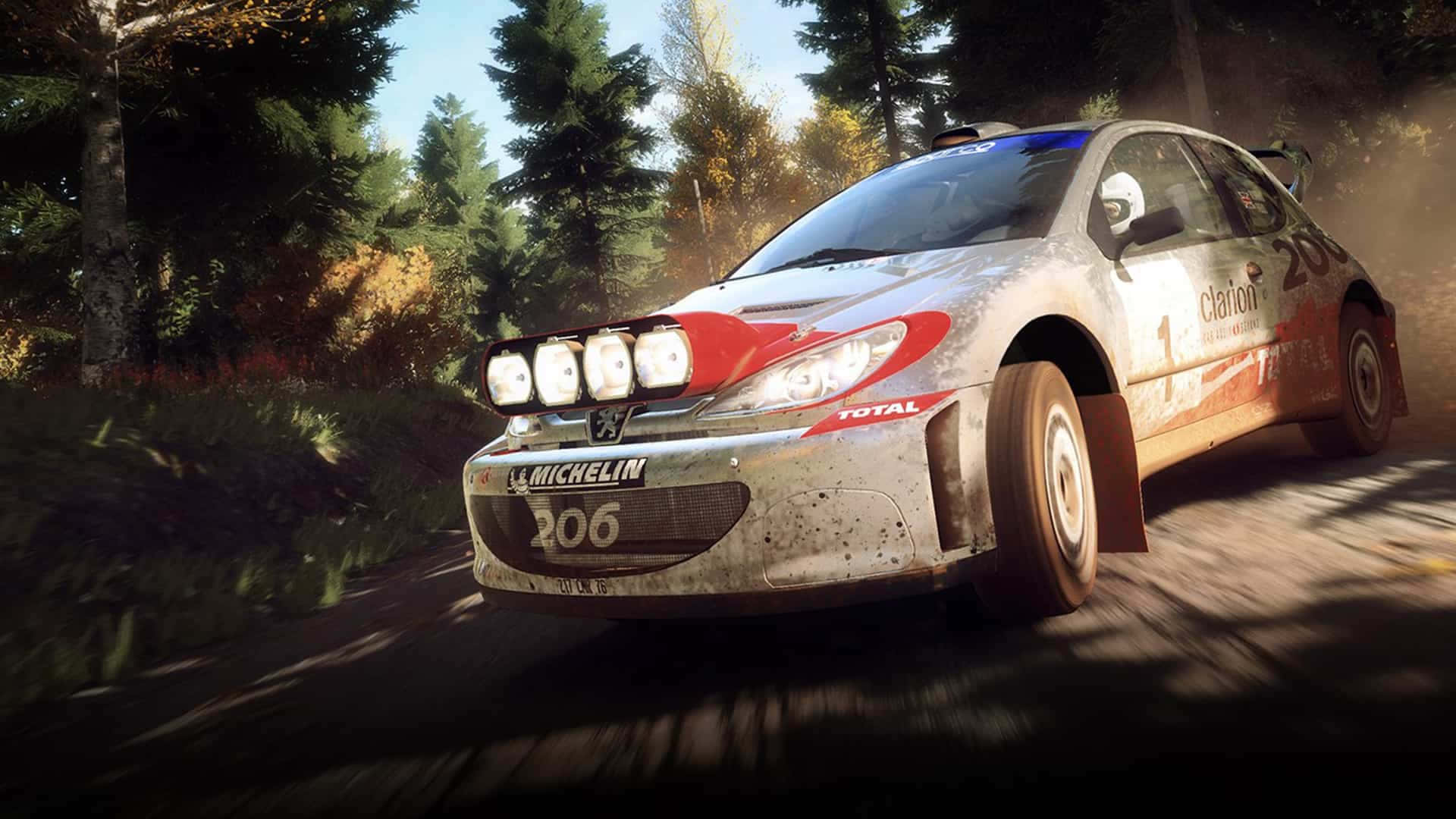 1920x1080 Dirt Rally 桌布 壁紙 — 一輛泥濘的拉力賽車在明亮的陽光下，飛馳在森林中的泥路上，揚起灰塵。