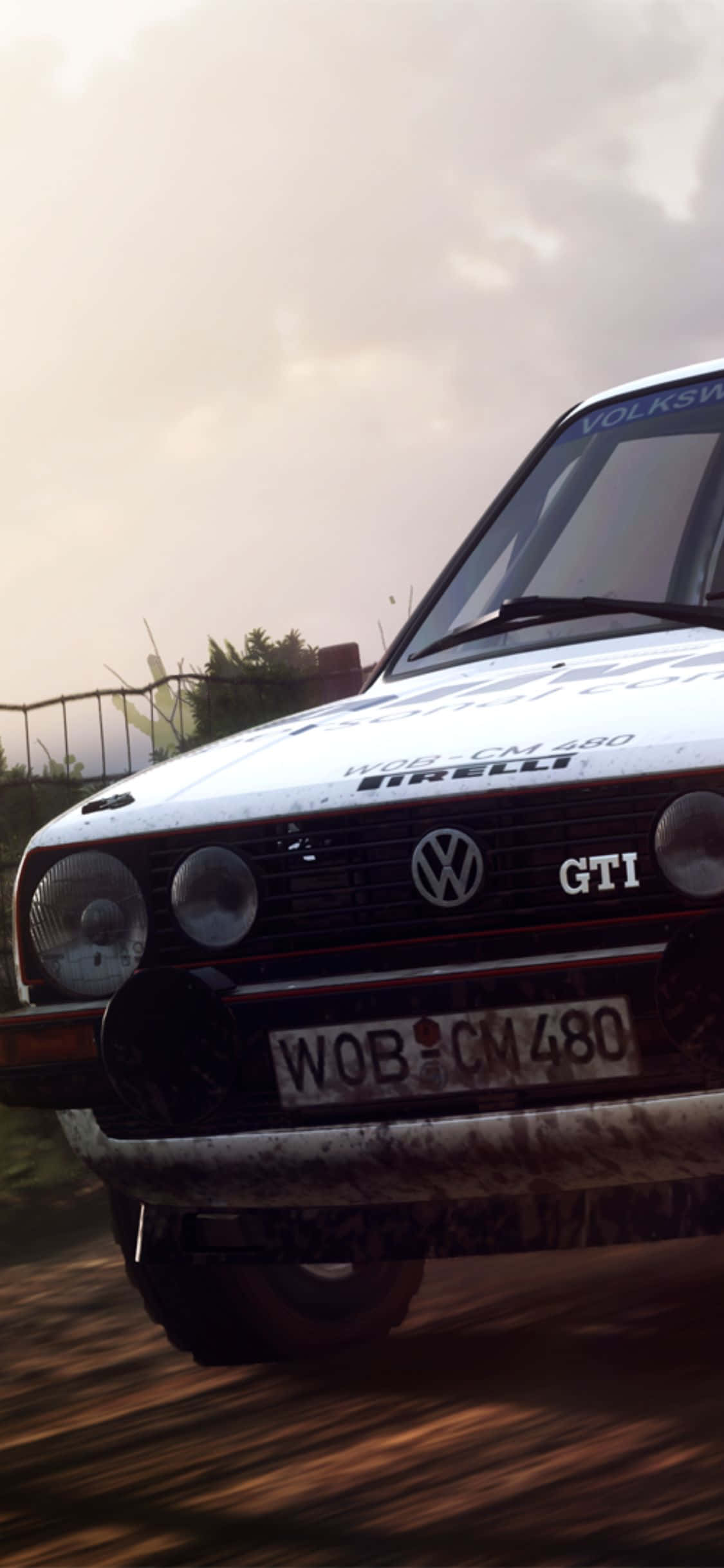 iPhone X Dirt Rally 桌布 壁紙 — 一輛泥濘的白色福斯 GTI 拉力賽車在多雲的天空下疾馳穿過森林泥路。