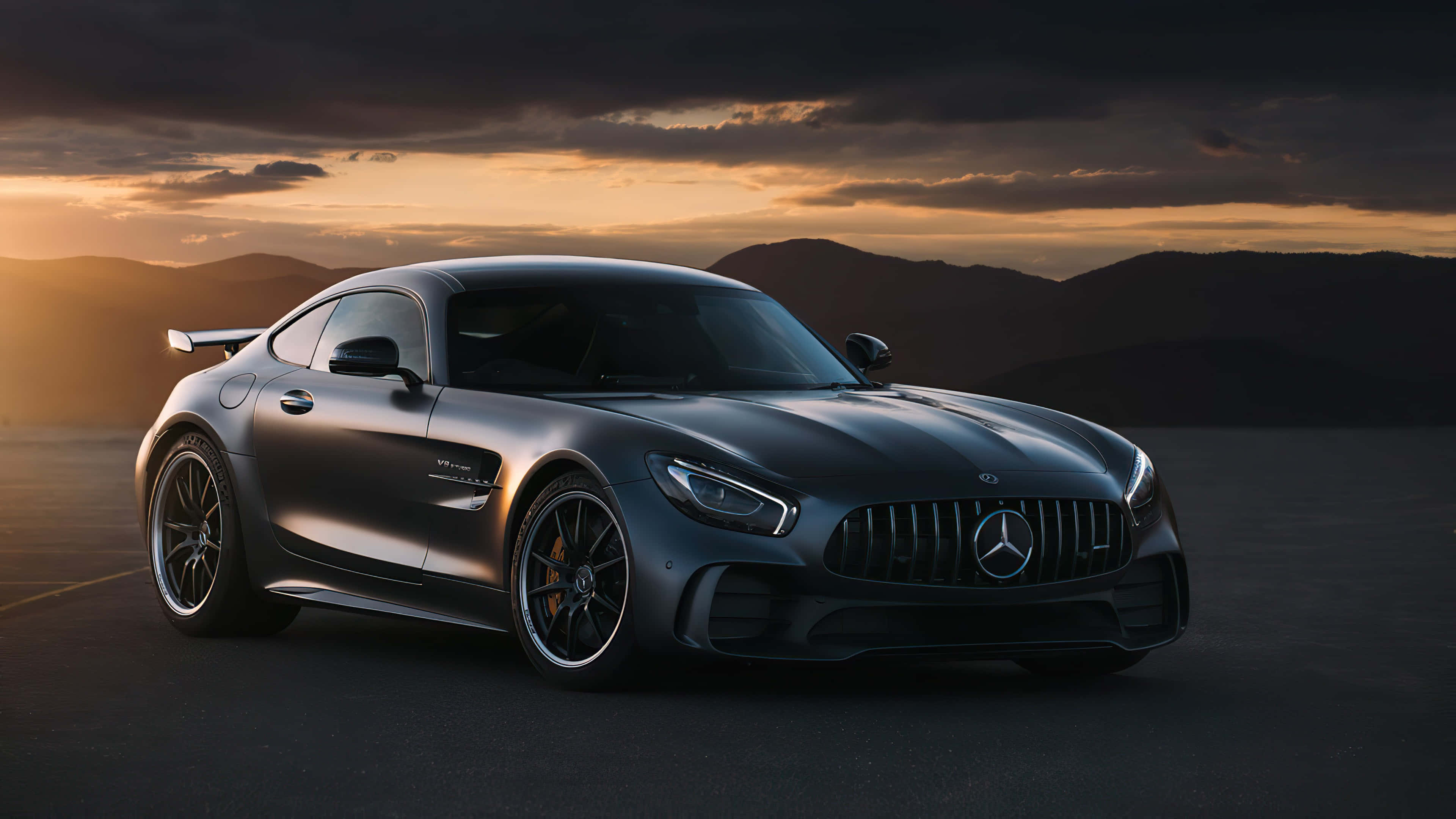 4K 奔馳壁紙 桌布 壁紙 — 一輛流線型啞光灰色Mercedes-AMG GT停泊在沙漠公路上，背景是日落時分的戲劇性雲層和遠山。
