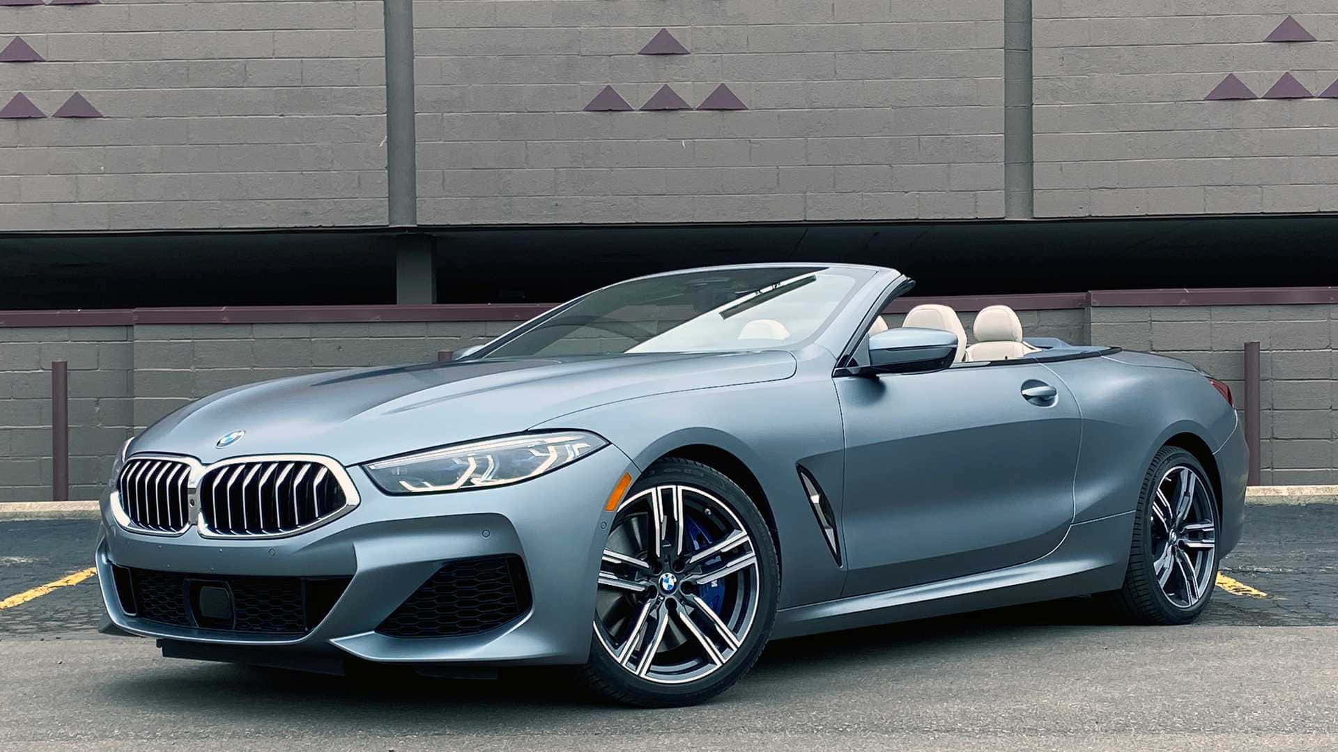BMW 動圖 桌布 壁紙 — 一輛流線型啞光灰色寶馬敞篷車停放在帶有三角形裝飾的灰色磚牆前。