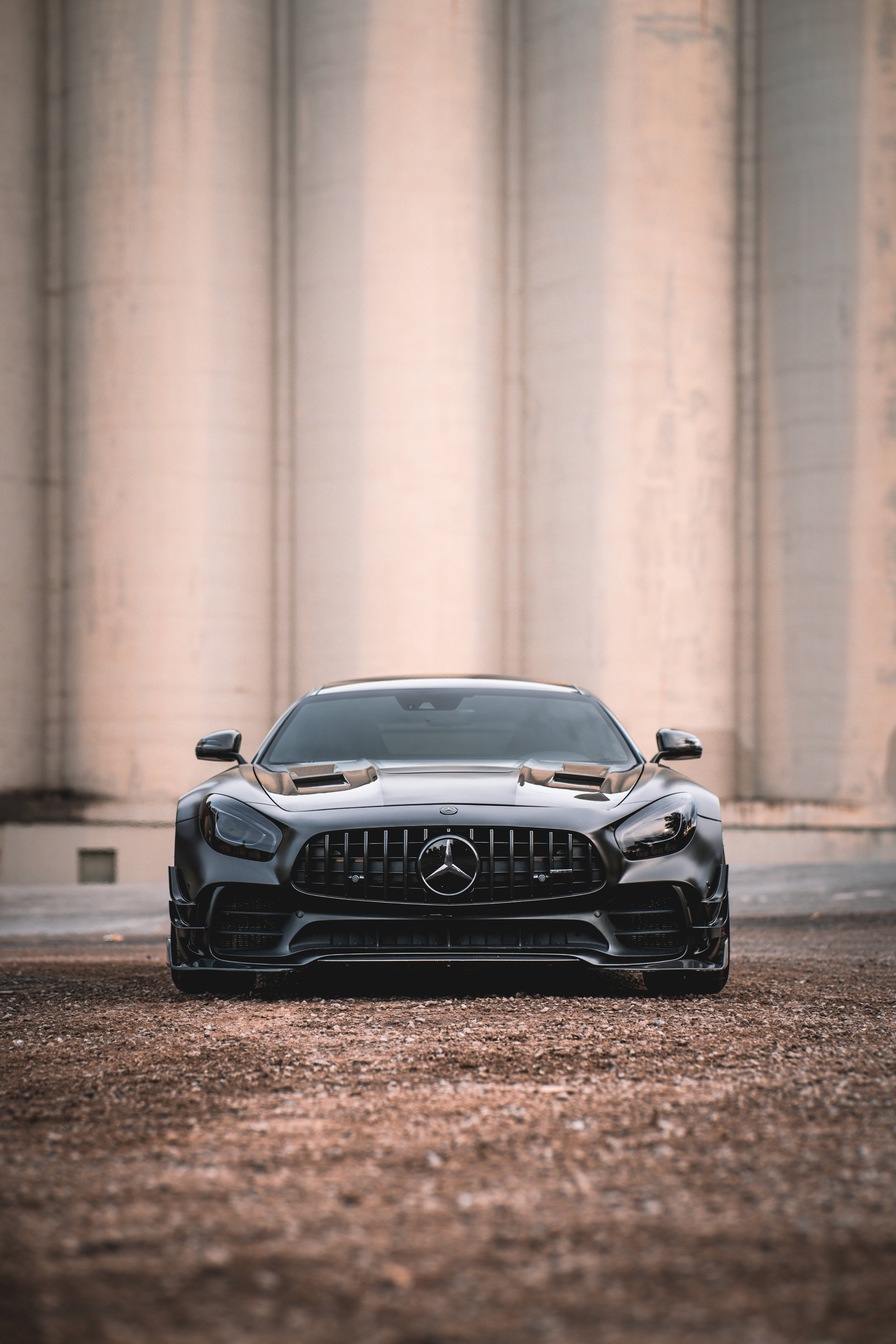 Gtr 桌布 壁紙 — 一輛流線型啞黑色 Mercedes-AMG GT R 跑車在巨型混凝土柱前的礫石上正面朝前。