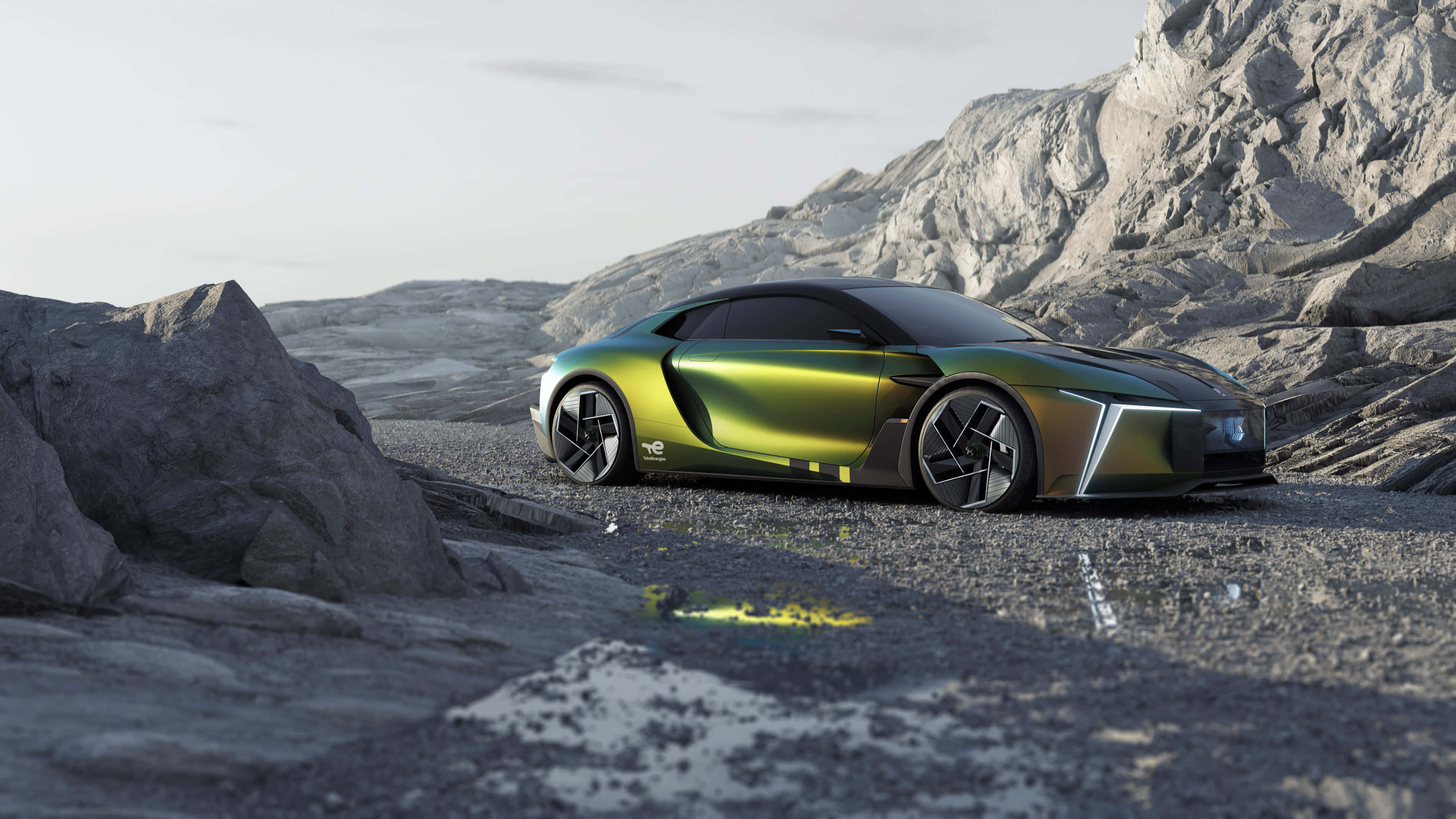 Ds Automobiles 桌布 壁紙 — 一輛流線型未來感綠色跑車停放在岩石地形上，背景是鋸齒狀山脈，天空蒼白。