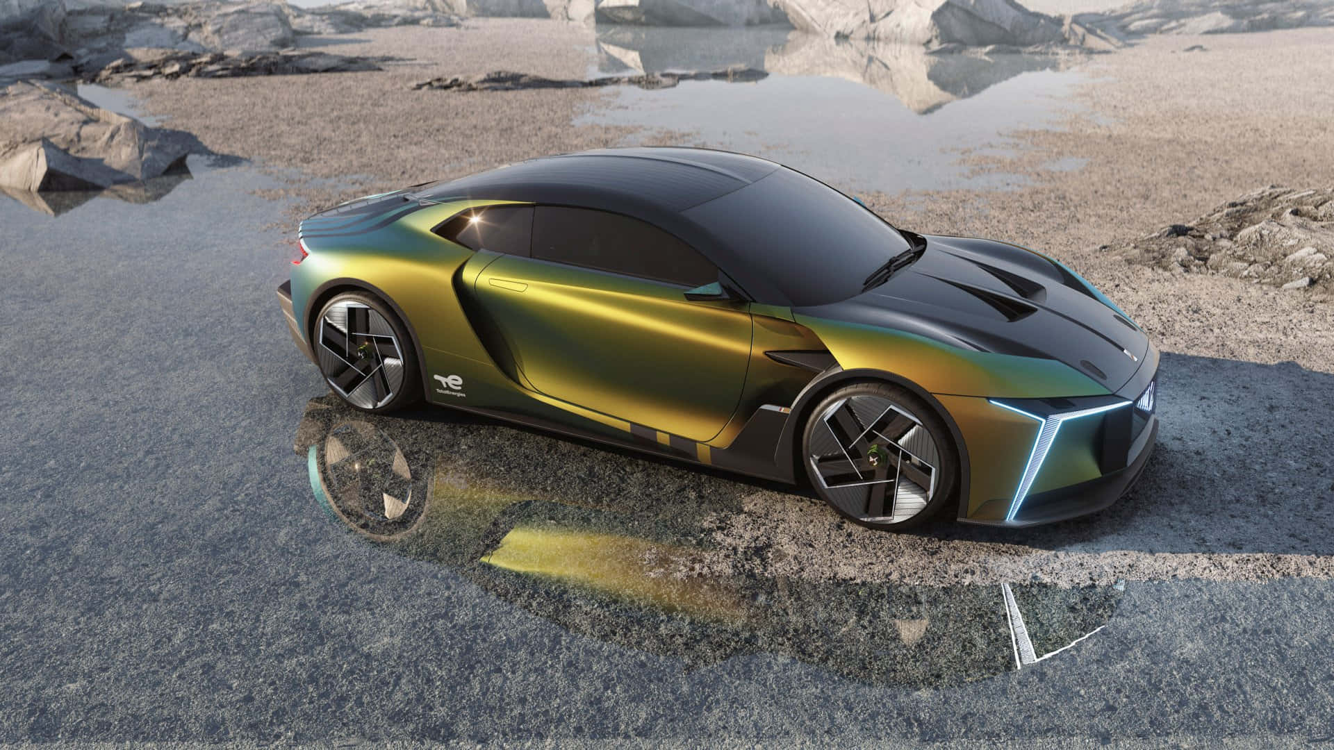 Ds Automobiles 桌布 壁紙 — 一輛流線型未來感跑車，帶有虹彩金黑漆面，停在濕混凝土上，在岩石地形附近反射出藍色光芒。