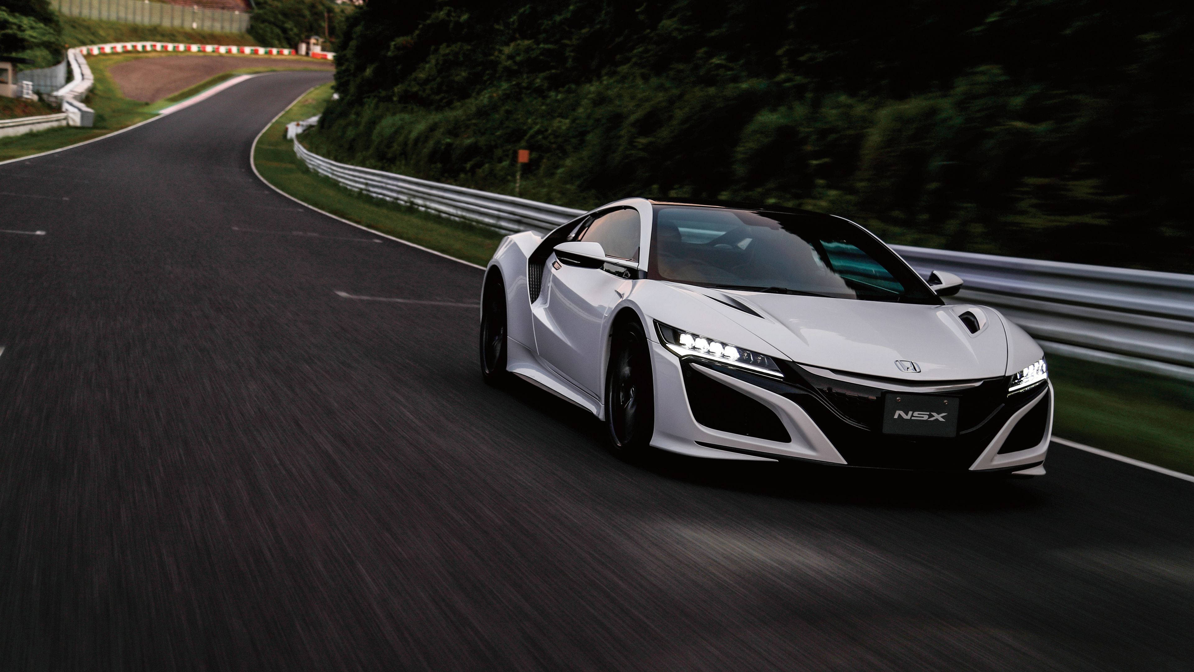 汽車 4K 桌布 壁紙 — 一輛流線型白色Acura NSX跑車在蜿蜒的瀝青路上奔馳，兩旁是茂密的綠樹和護欄。