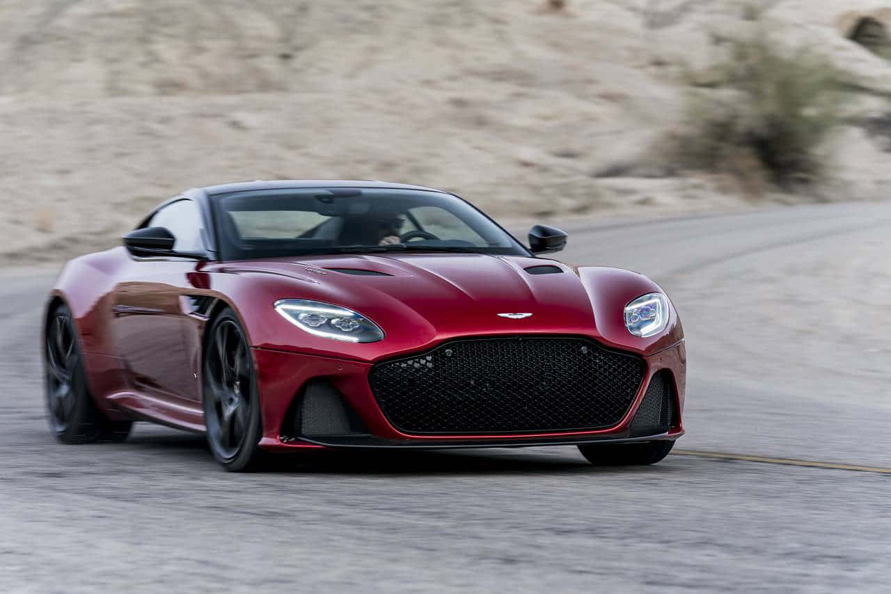 奧斯頓馬丁 桌布 壁紙 — 一輛流線型的紅色Aston Martin跑車在蜿蜒的沙漠公路上疾馳，帶有模糊的動感。