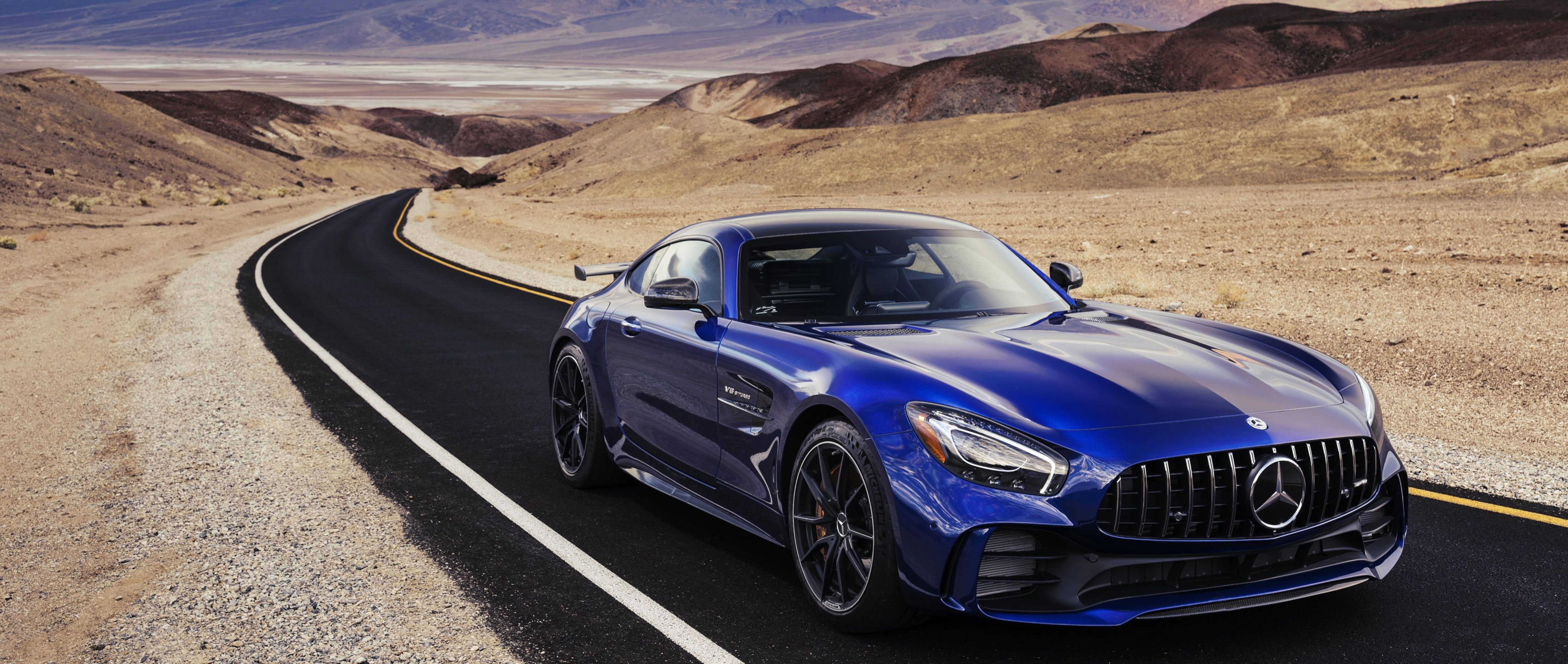 藍色 Mercedes-AMG GT 在沙漠公路上，背景有山脈。 — 4K 奔馳壁紙 壁紙