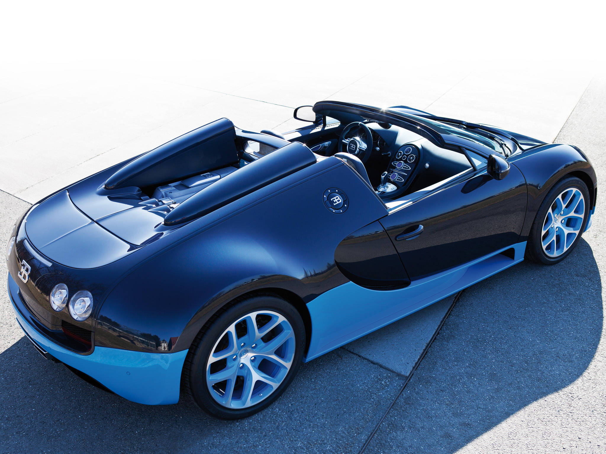 bugatti iPhone 桌布 壁紙 — 一輛流線型的藍黑 Bugatti Veyron Super Sport 敞篷車停在陽光普照的混凝土上。