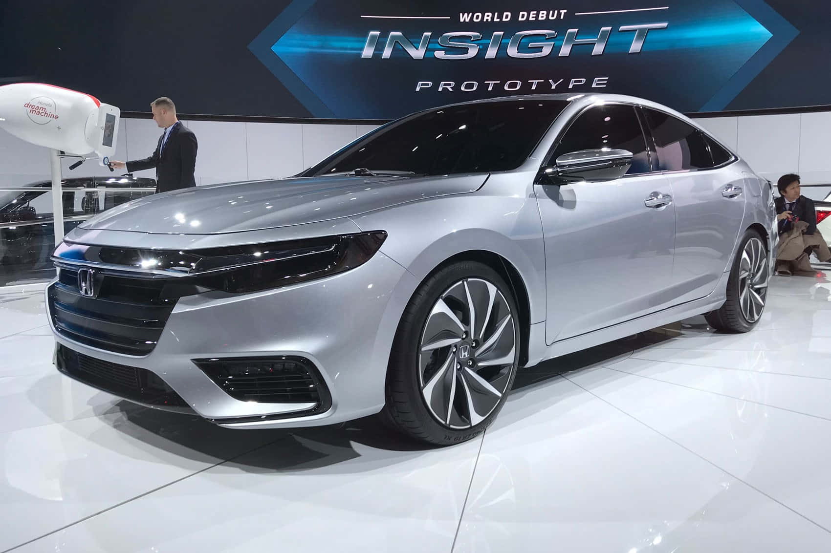 Honda Insight 桌布 壁紙 — 一輛流線型的銀色本田Insight原型車在車展的明亮燈光下閃閃發光，背後有一個大型顯示螢幕。