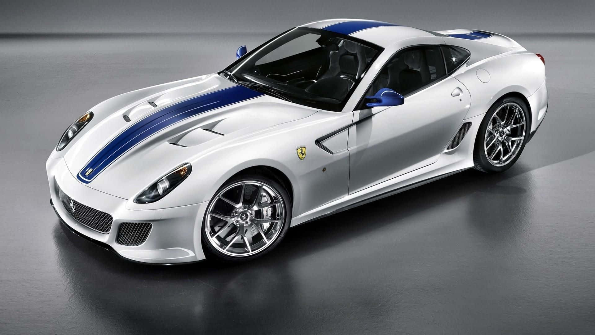 Ferrari 599 Gtb Fiorano 桌布 壁紙 — 一輛流線型的銀色法拉利跑車，帶有醒目的藍色賽車條紋，在攝影棚燈光下於反光的灰色地板上閃閃發光。