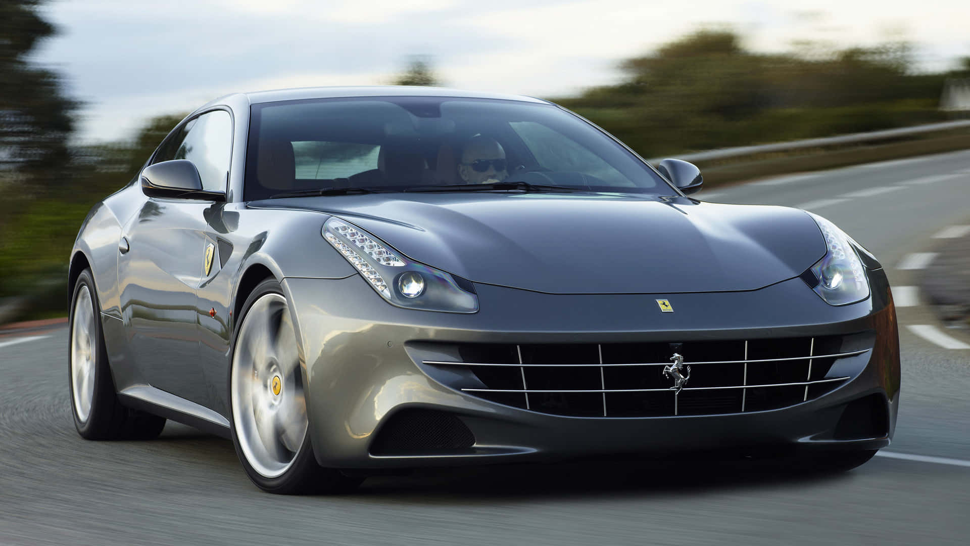 Ferrari Ff 桌布 壁紙 — 一輛流線型的銀色法拉利跑車在蜿蜒的道路上奔馳，背景是模糊的綠意。