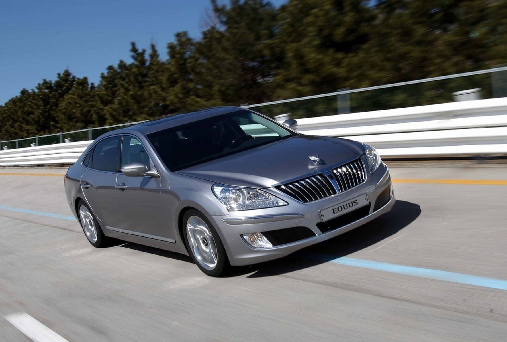 Hyundai Equus 桌布 壁紙 — 一輛流線型的銀色現代Equus轎車在陽光明媚的高速公路上疾馳，兩旁是茂密的綠樹和白色護欄。