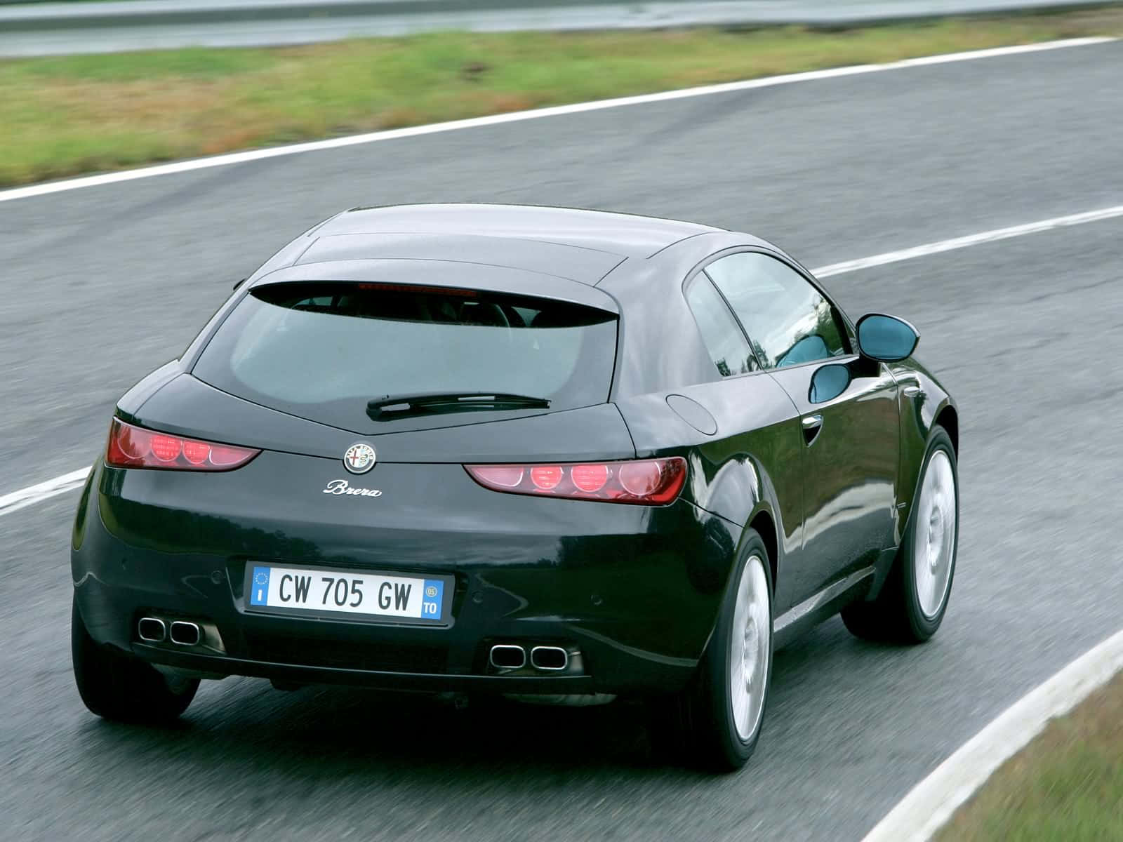 Alfa Romeo Brera 桌布 壁紙 — 一輛流線型的黑色愛快羅密歐 Brera 跑車在濕滑的瀝青路上疾馳，路旁有模糊的綠色草地和白色車道標線。