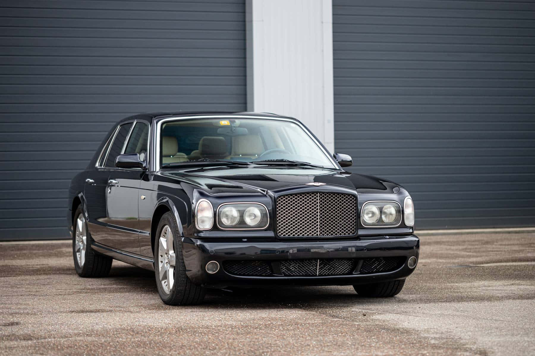 Bentley Arnage 桌布 壁紙 — 一輛流線型的黑色賓利 Arnage 停放在灰色工業車庫門前的混凝土場地上。