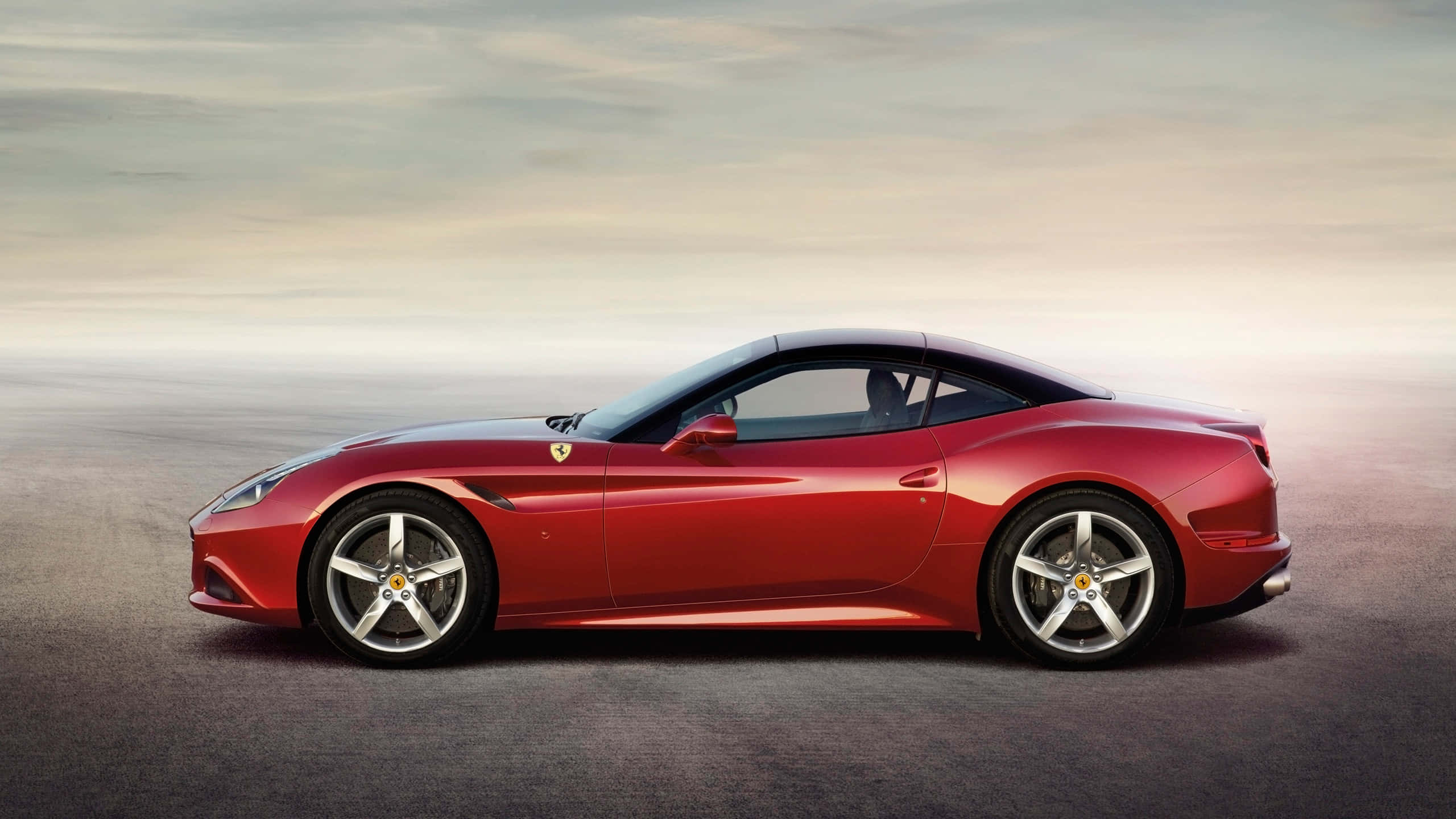 Ferrari California T 桌布 壁紙 — 一輛流線型紅色法拉利跑車在平滑的灰色表面上滑行，天空呈現柔和漸變色。