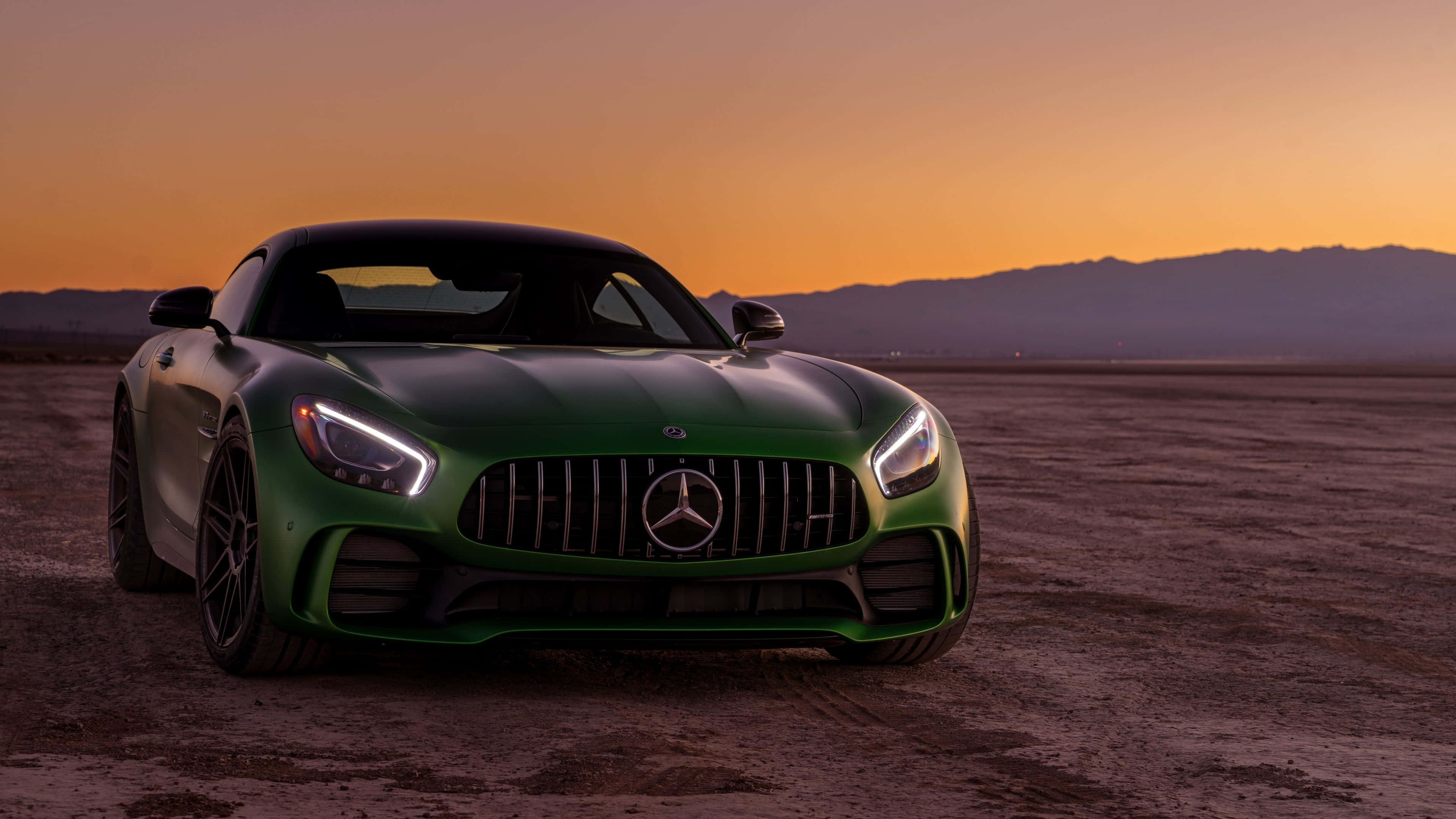 Mercedes 桌布 壁紙 — 一輛流線型綠色Mercedes-AMG GT跑車在溫暖的日落天空下閃閃發光，背景是遠山。