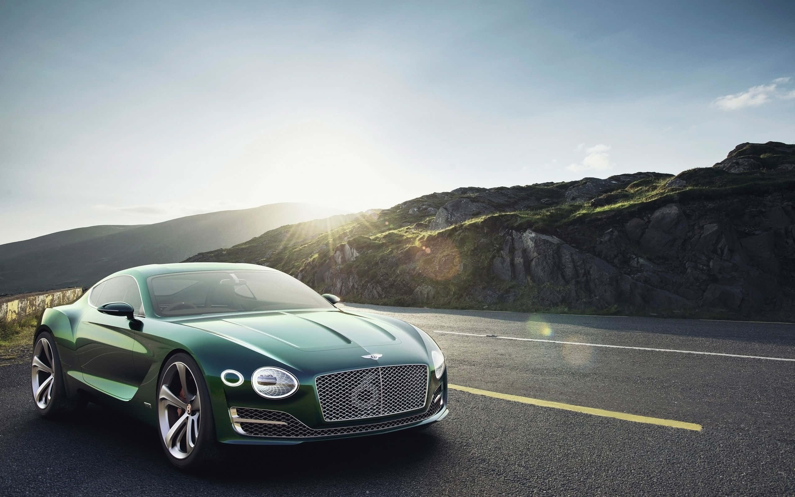 Best Bentley 桌布 壁紙 — 一輛流線型綠色賓利跑車沿著蜿蜒的山路行駛，沐浴在金色的夕陽光芒中。