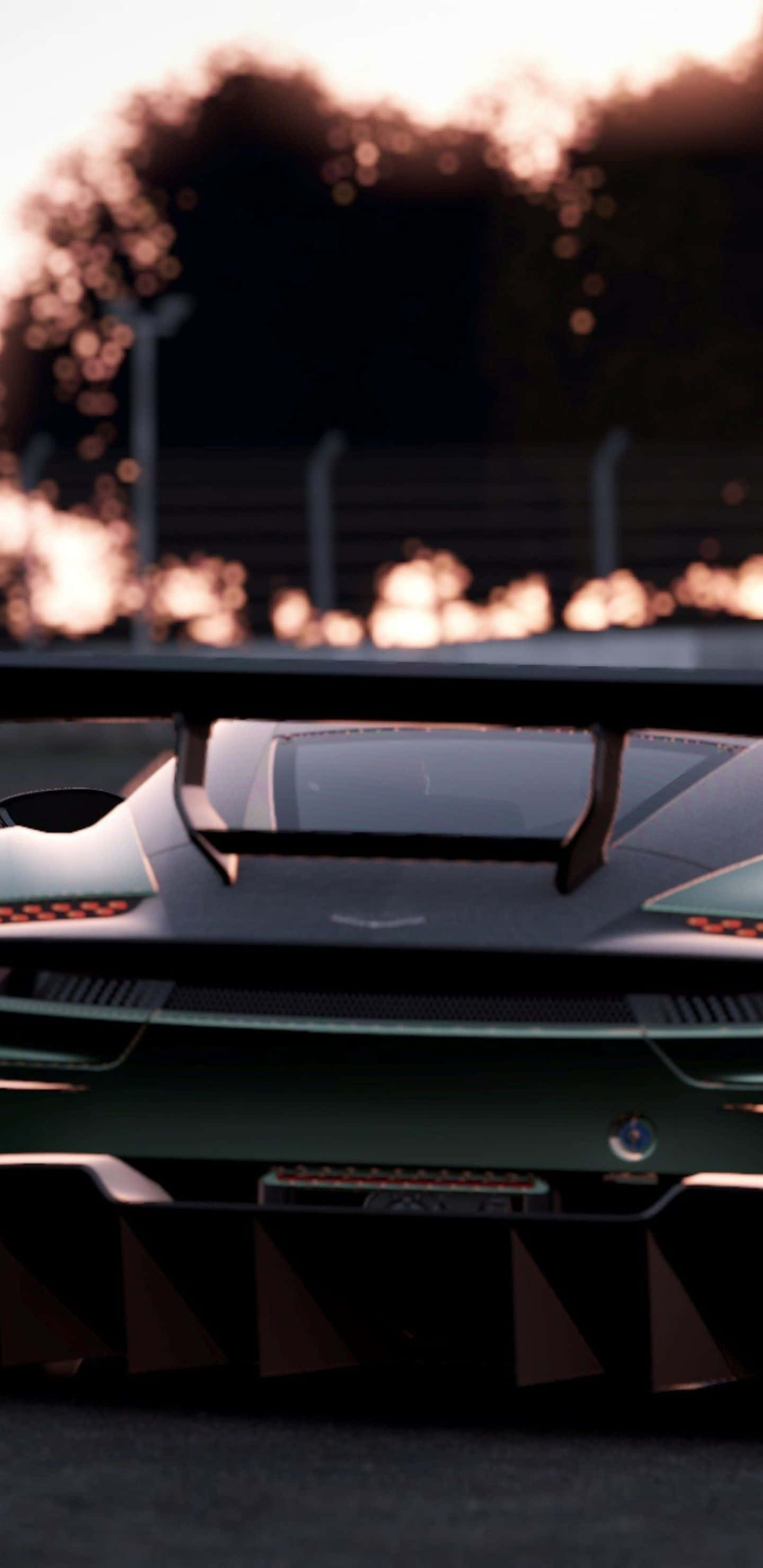 Pixel 3xl Project Cars 2 桌布 壁紙 — 一輛流線型綠色賽車的車尾在金色日落光線下閃耀，賽道上有模糊的樹木和護欄。