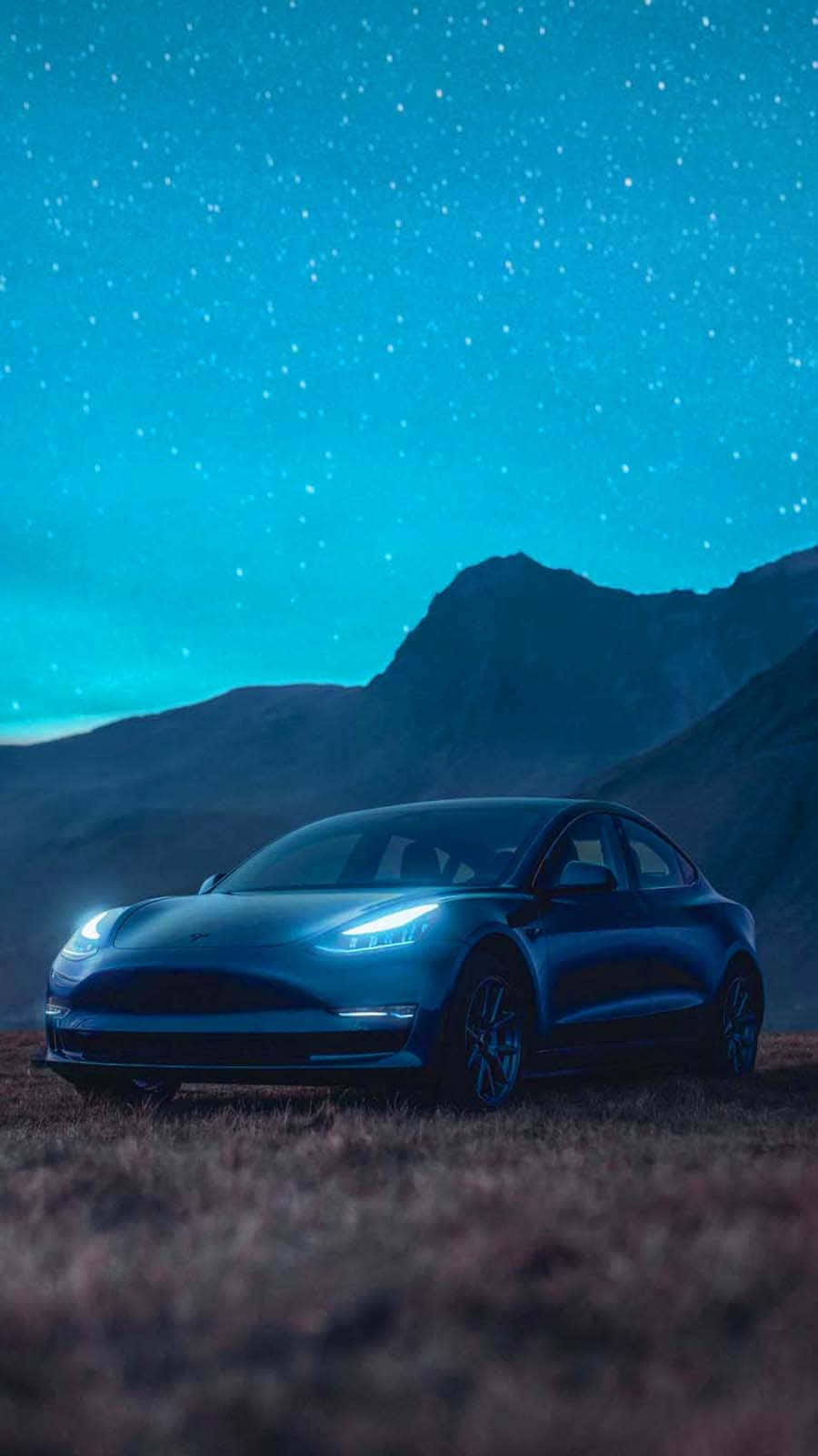 特斯拉 桌布 壁紙 — 一輛流線型藍色 Tesla Model 3 停泊在草地上，背景是星空和黑暗的山脈。