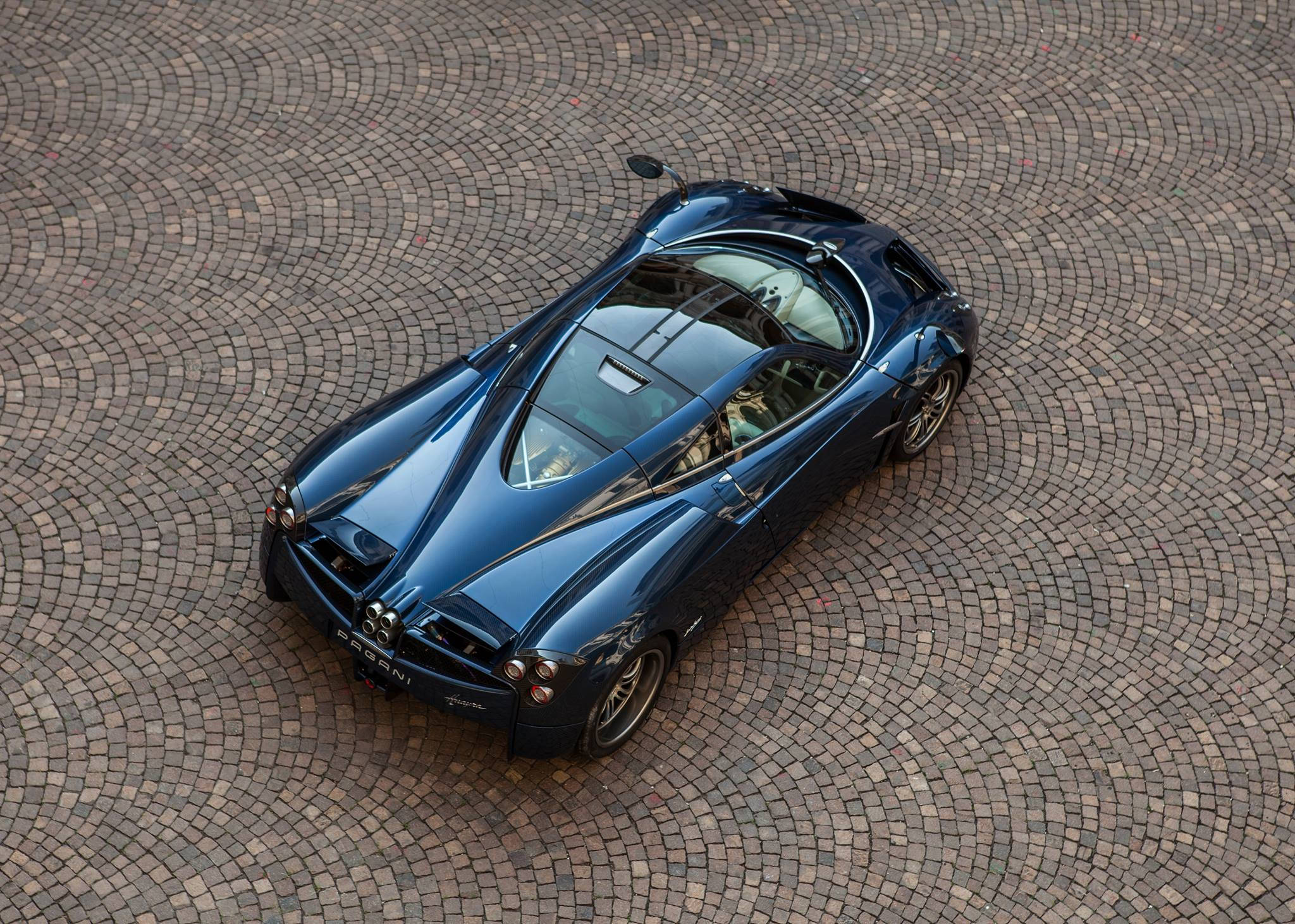 Pagani 桌布 壁紙 — 一輛流線型藍色Pagani跑車在明亮日光下停放在彎曲的鵝卵石路面上。