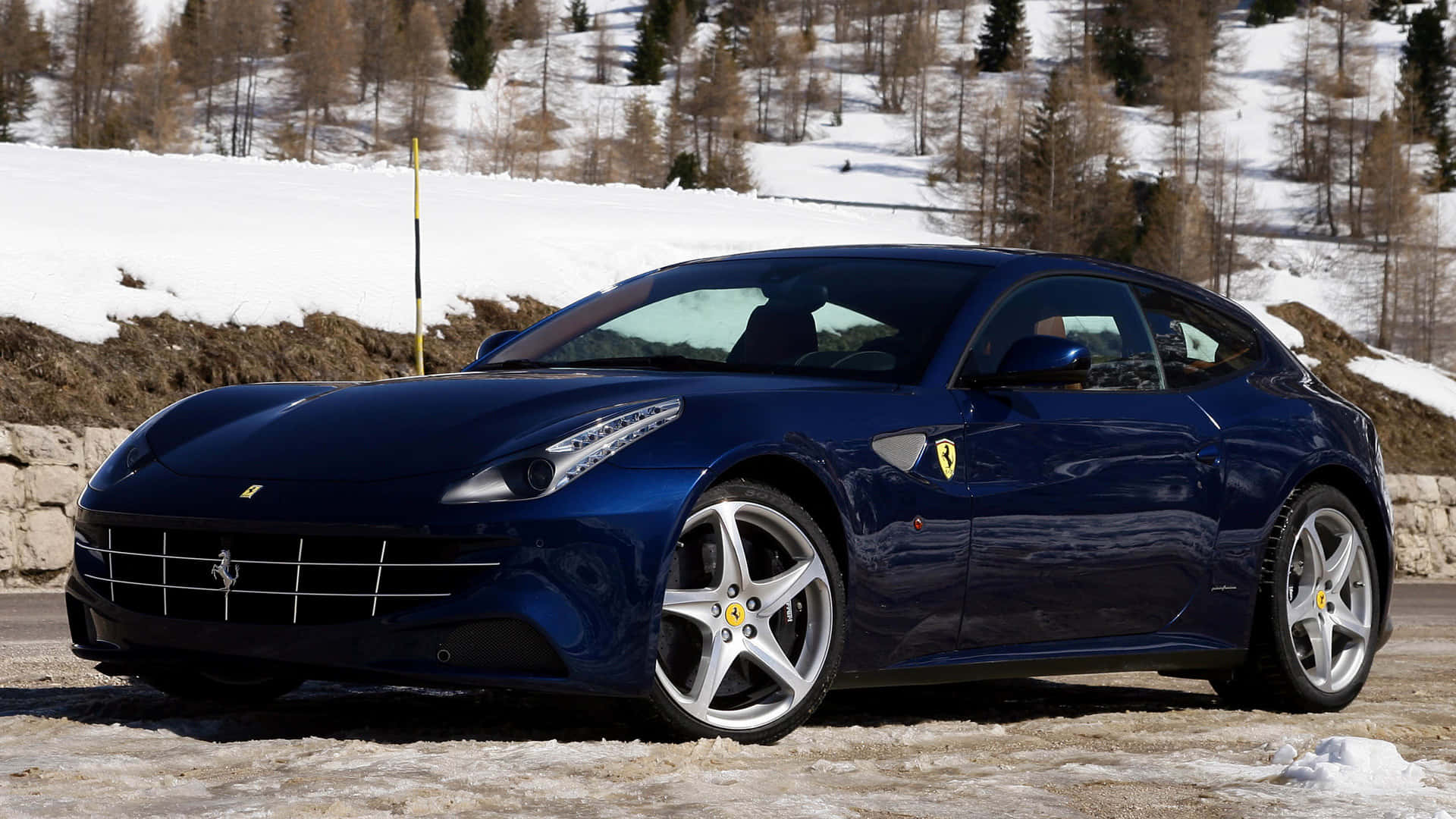 Ferrari Ff 桌布 壁紙 — 一輛流線型藍色法拉利跑車停放在積雪的路邊，背景是白雪覆蓋的樹木和山丘。